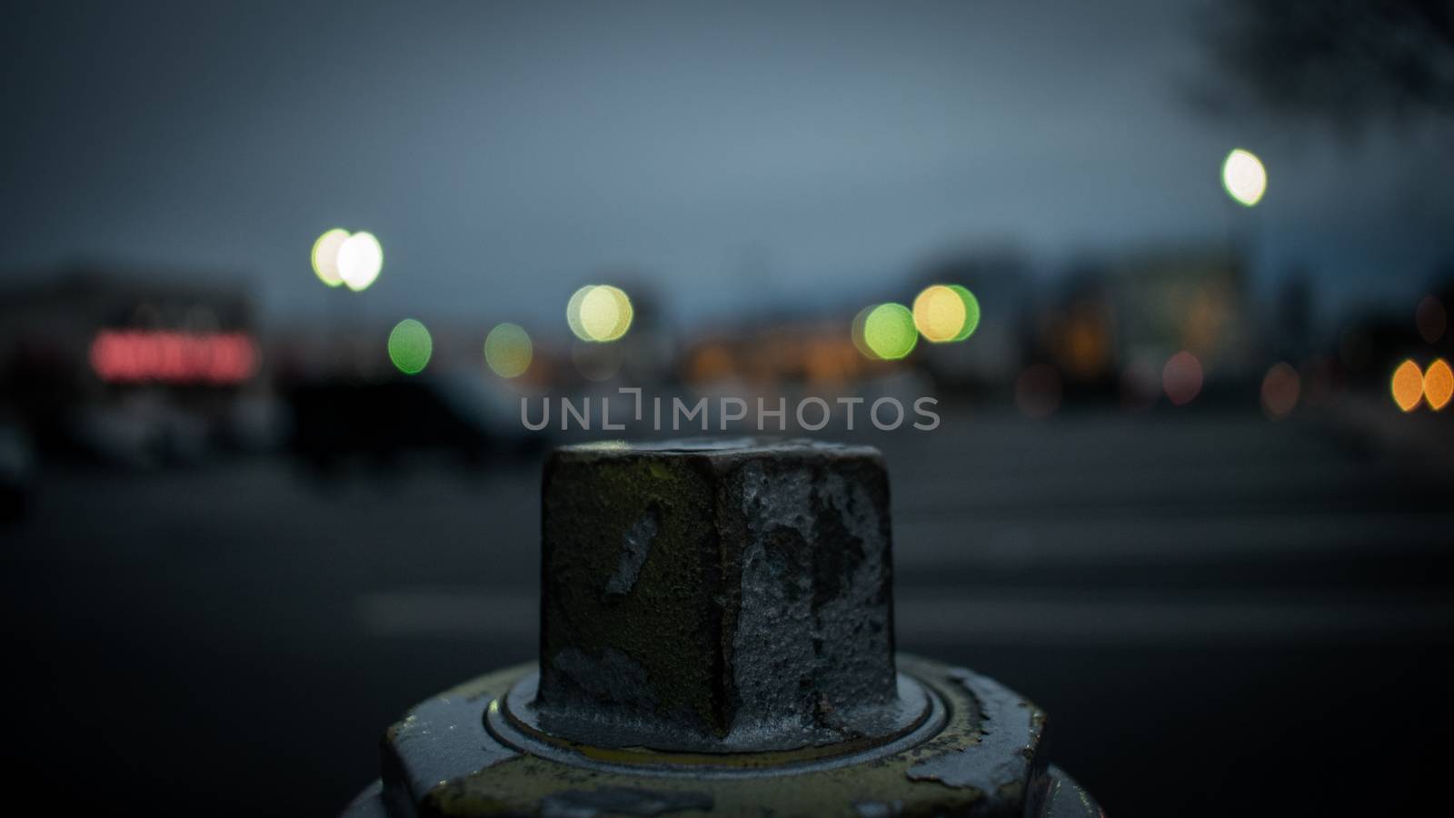 The Top of a Fire Hydrant With a Blurred Shopping Center Behind  by bju12290