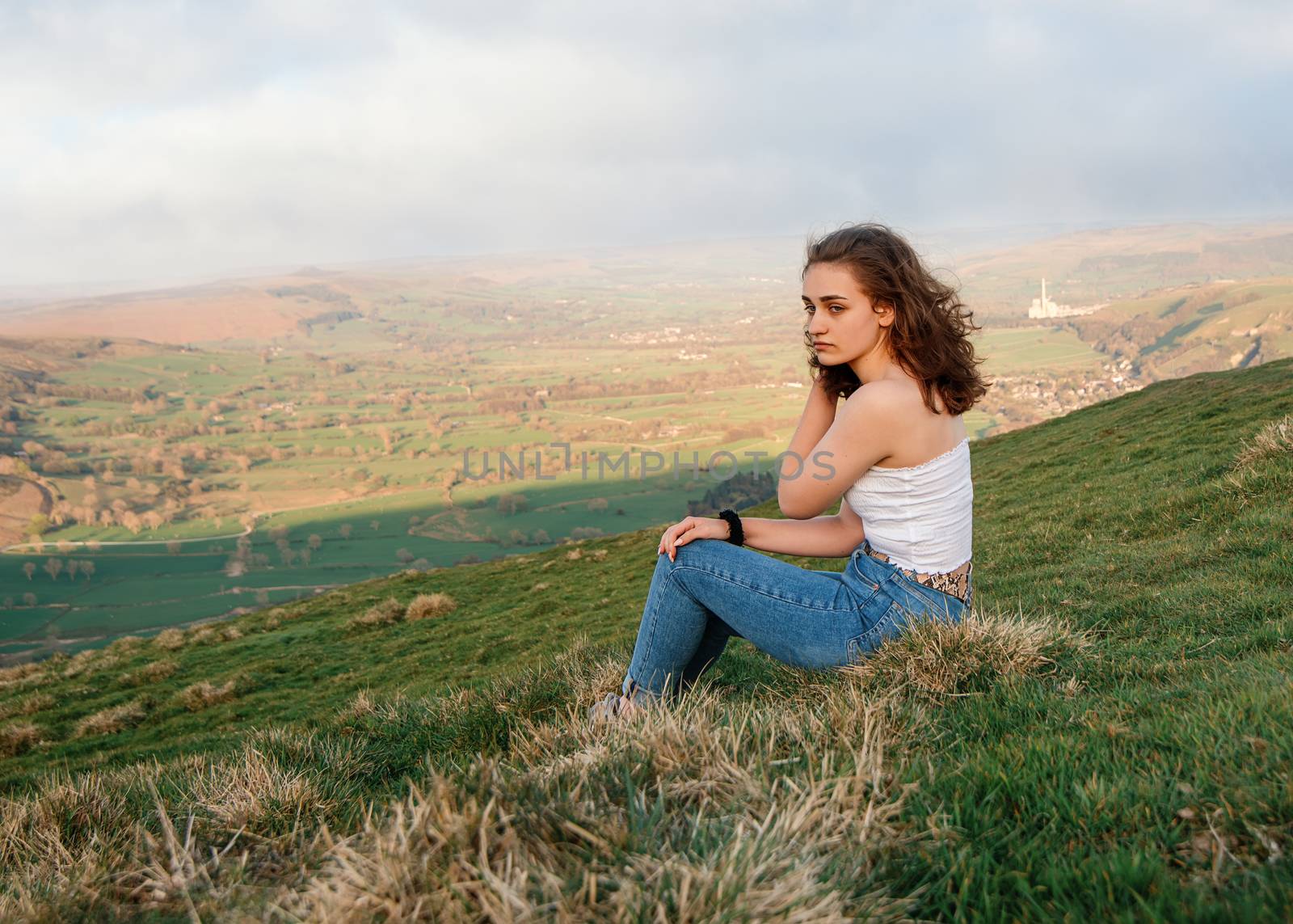 A girl sitting on top of the hill against amazing landscape in the summer