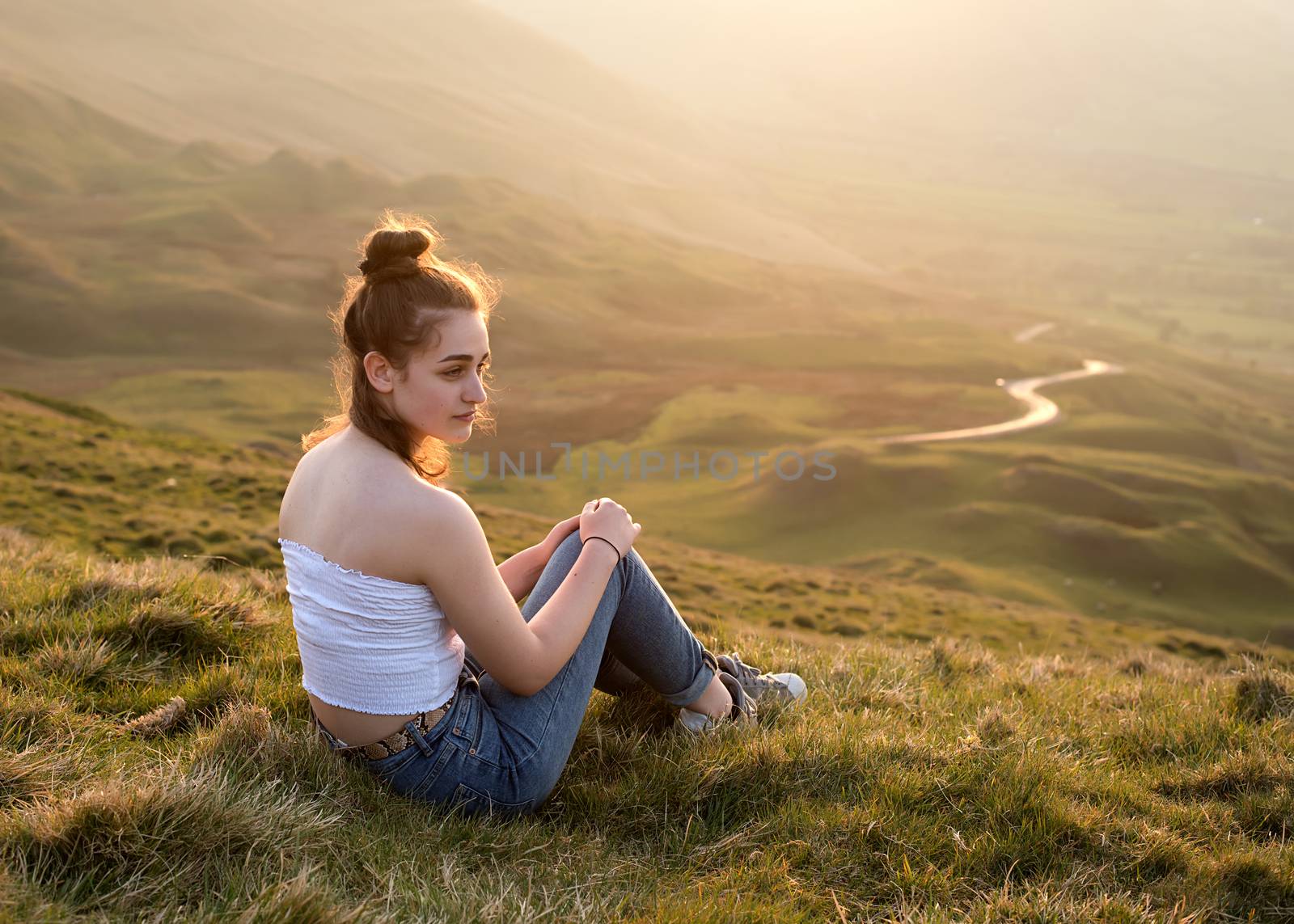 A girl sitting on top of the hill against amazing landscape at s by Iryna_Melnyk