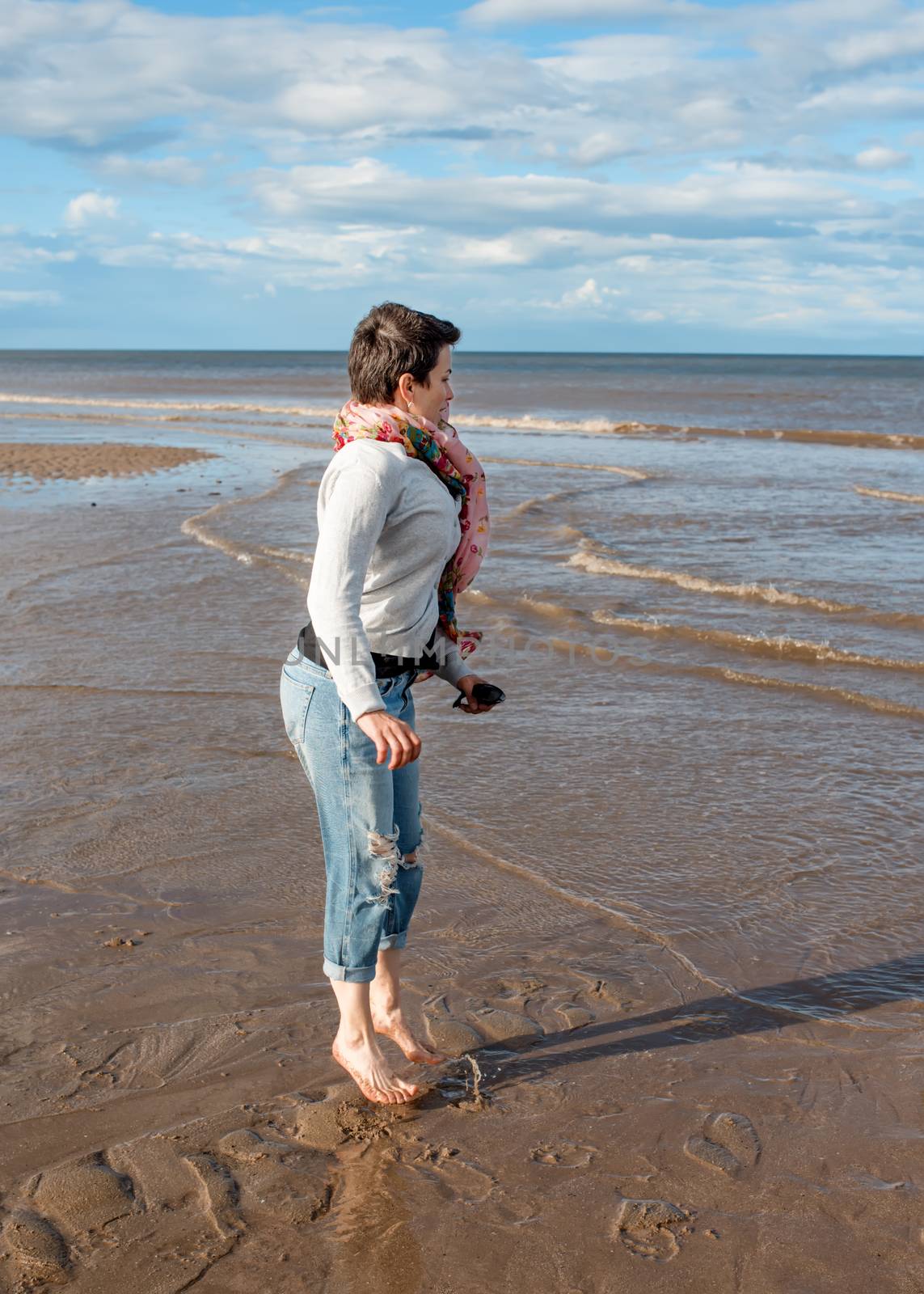 Barefoot woman wearing jeans and grey jumper jumping on the beach