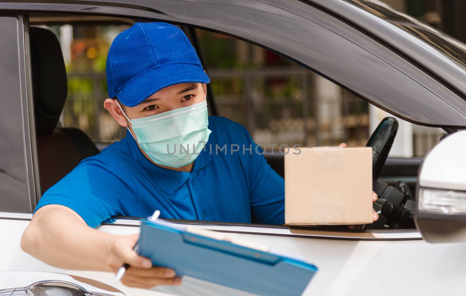 Asian delivery courier young man driver inside van car giving parcel post boxes to customer receiving both protective face mask, under curfew quarantine pandemic coronavirus COVID-19