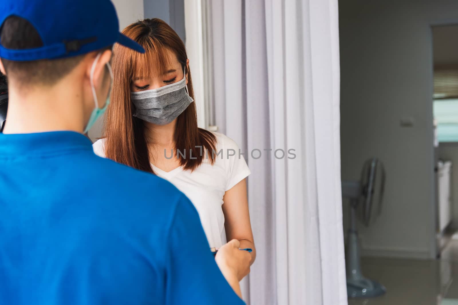 Asian young delivery man courier shopping online with package post box in uniform protective face mask coronavirus he making service woman customer using pen signature on paper book at home, COVID-19