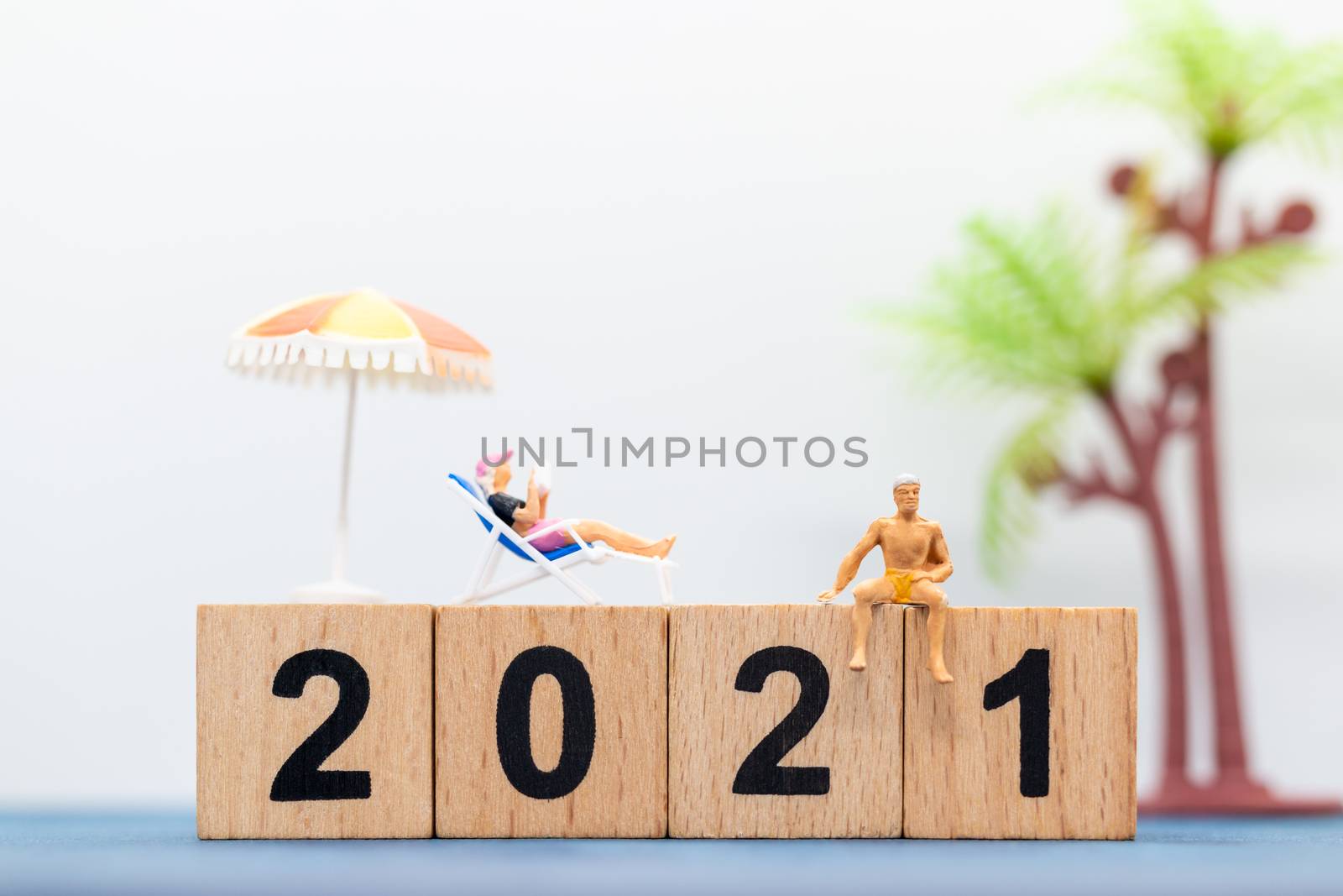 Miniature people wearing swimsuit sitting on the lounge chair at wooden block 2021