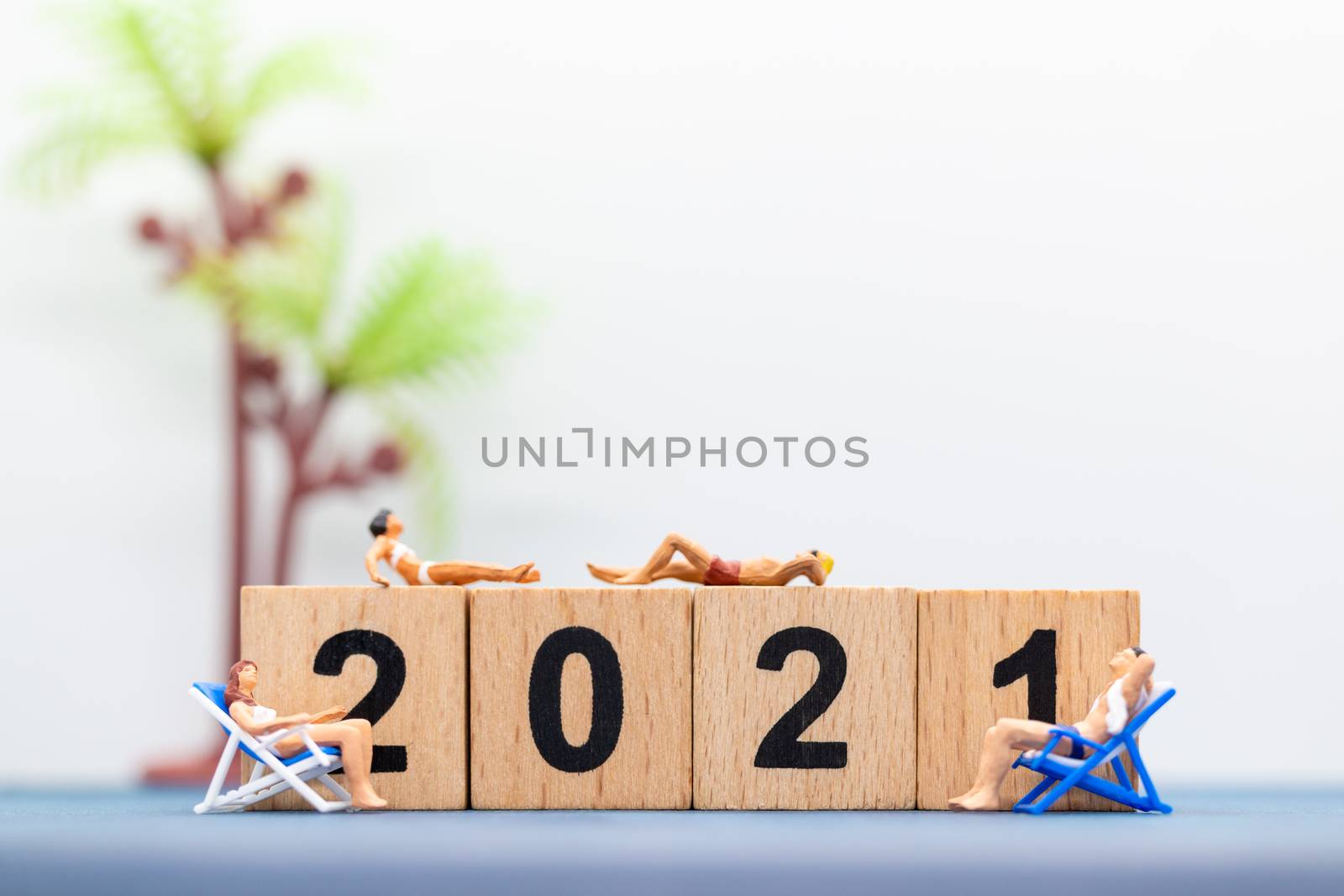 Miniature people wearing swimsuit sitting on the lounge chair at wooden block 2021