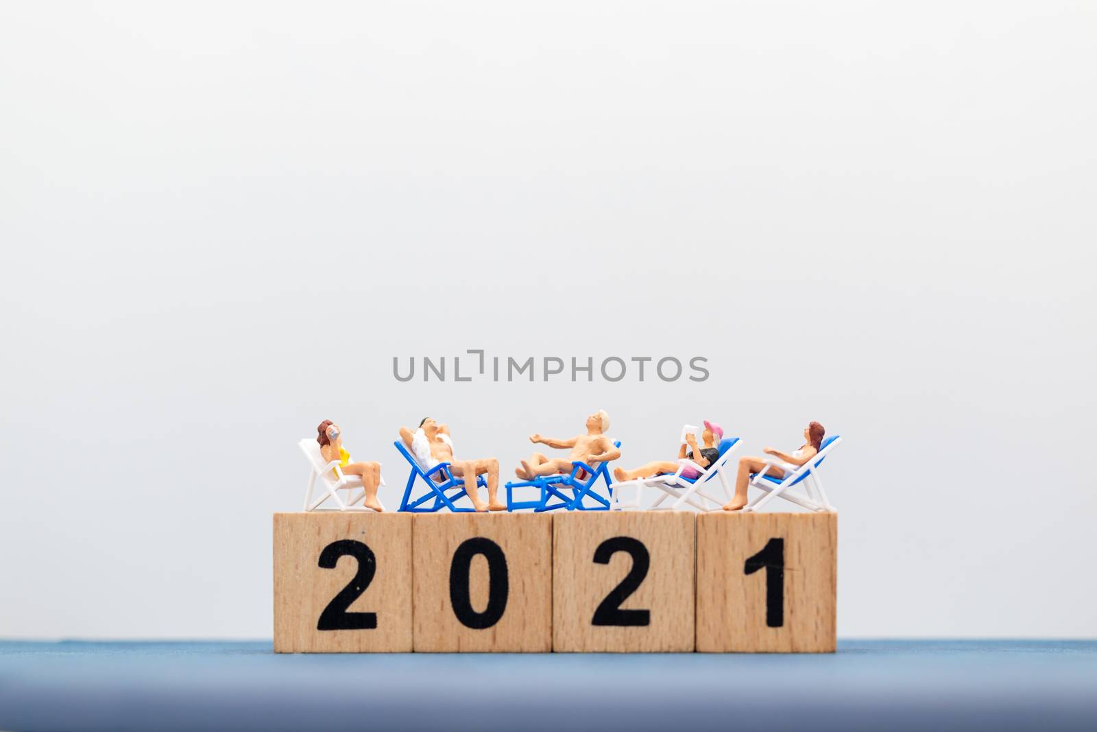 Miniature people wearing swimsuit sitting on the lounge chair at wooden block 2021