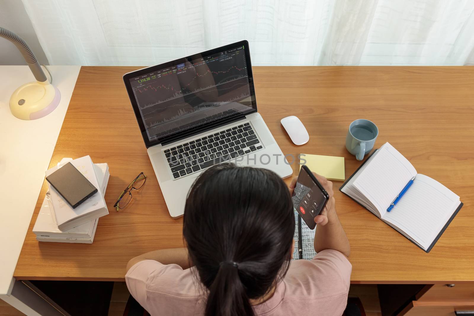 Top view business women use smart phone and laptop analysis stock market chart. Business people use laptop trade sell and buy stock market at home.