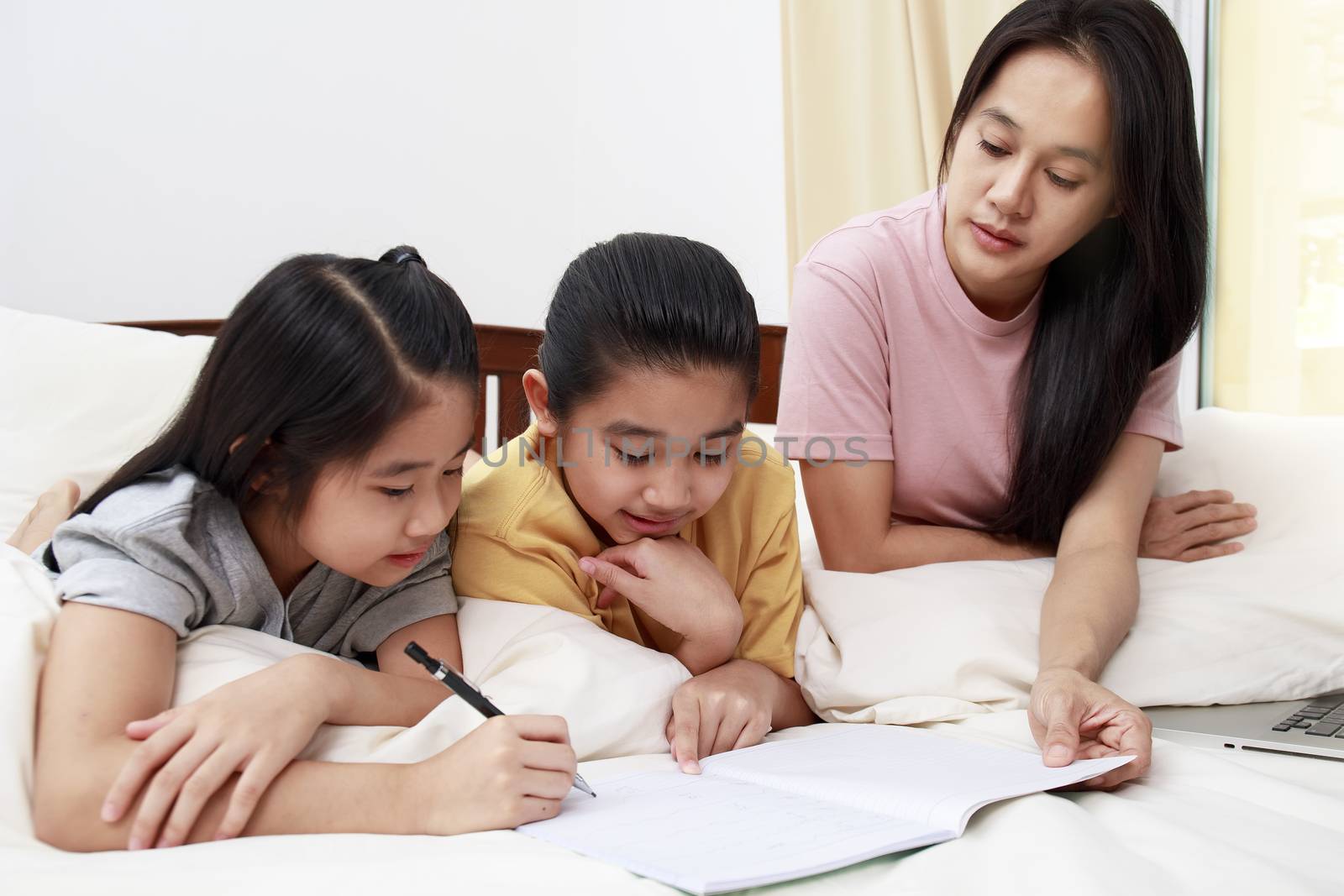 Asian family mother her daughters do homework  together on bed i by Satrinekarn