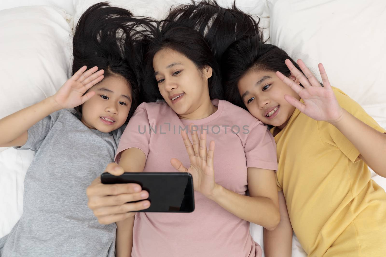 Close up happy mother and her kid making aselfie or video call to father in bed. Family concept mother and her daughter contact father with smarth phone by video call.