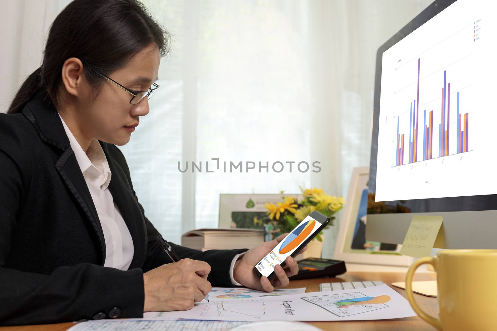 Business women holding smart phone check pie chart and write notes on desk at office. Business people analysis chart  report on phone and computer pc at home.