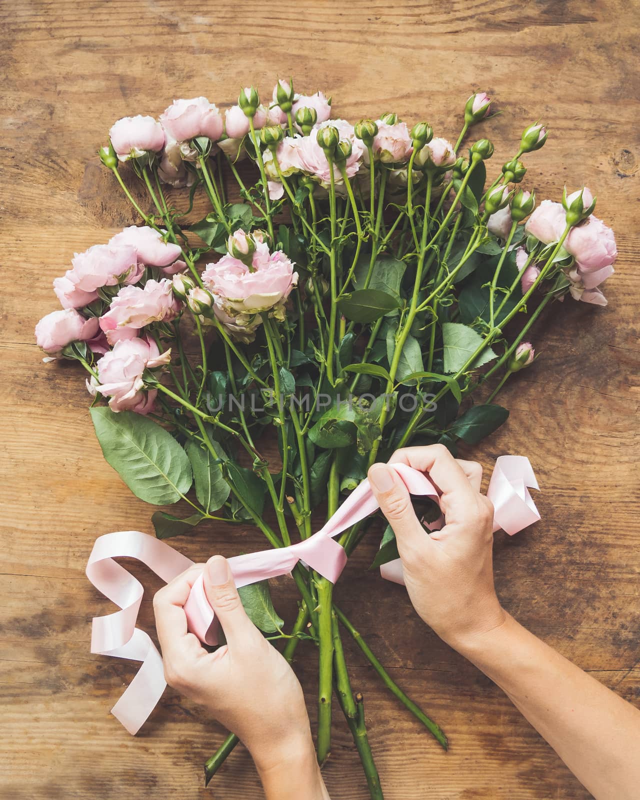 Top view on wooden table with roses and pink ribbon bow on it. Florist workplace. Accessories for making bouquets and floral compositions.