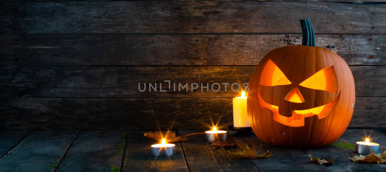 Halloween pumpkin head lantern burning candles and dry maple leaves on wooden background