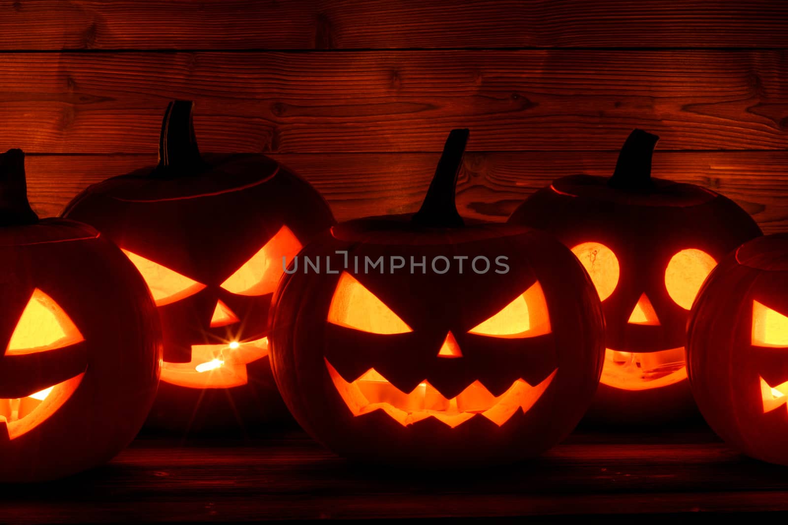 Row of Halloween pumpkin head lanterns with burning candles inside on wooden background