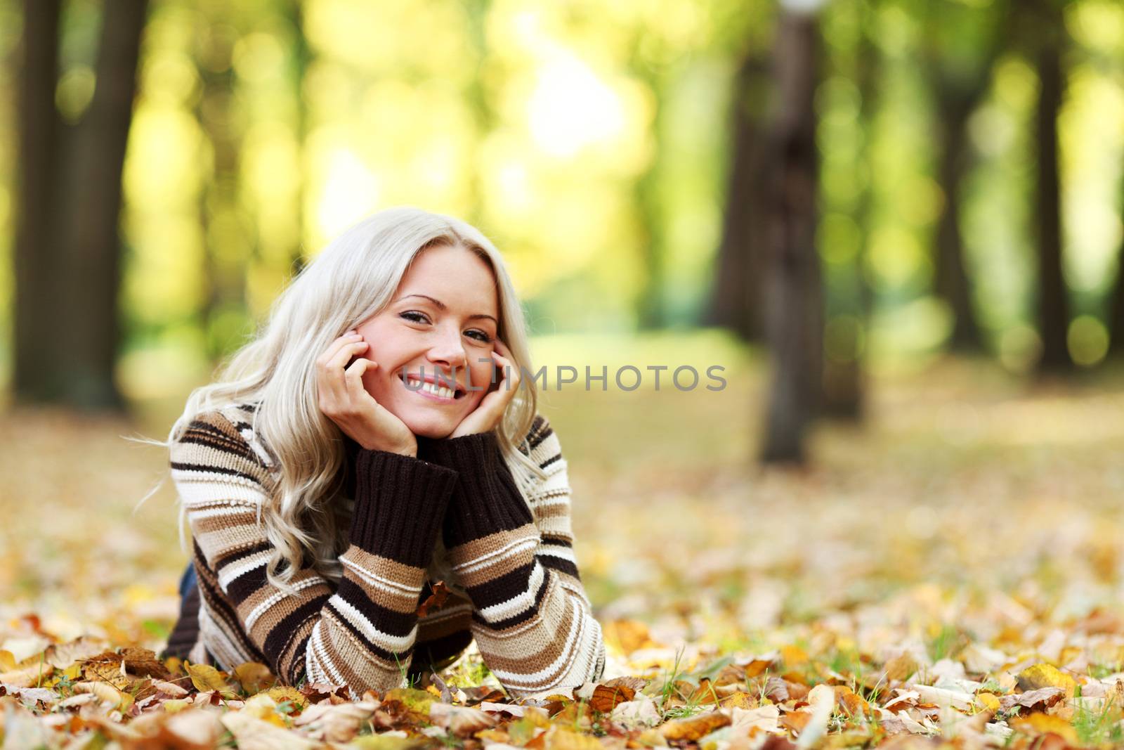 Portrait of young woman laying on ground with autumn leaves in park