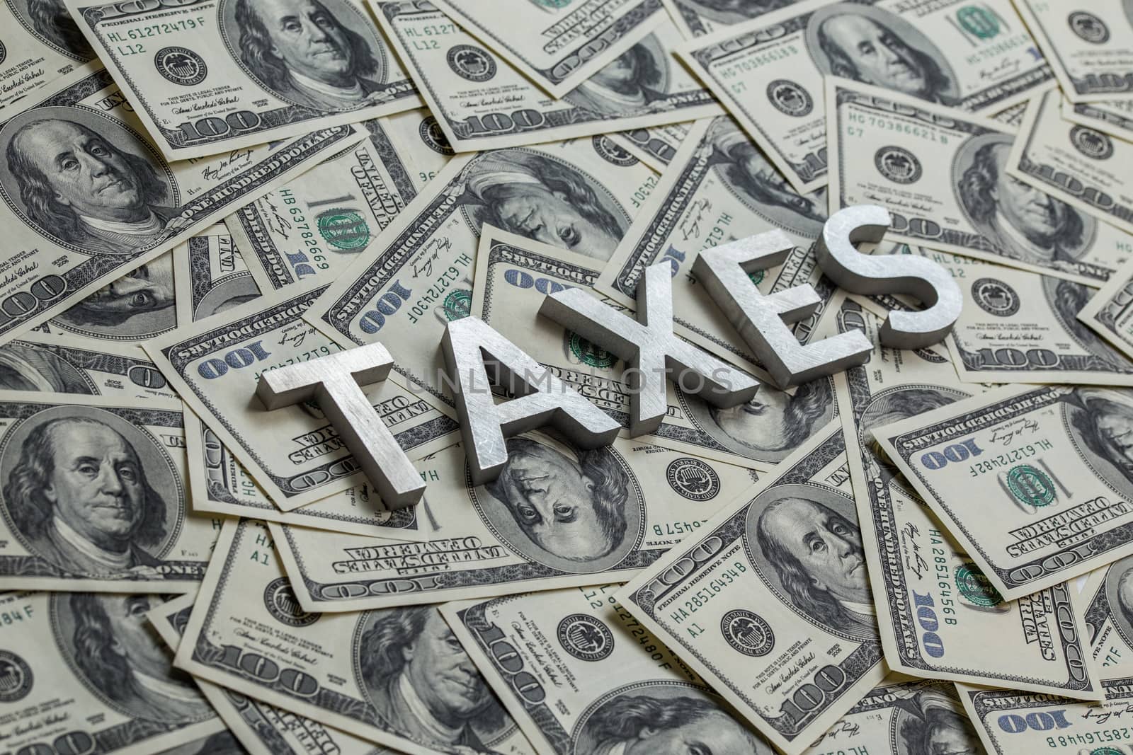 The word taxes with aluminium thick letters on the US dollar bills background - with selective focus.
