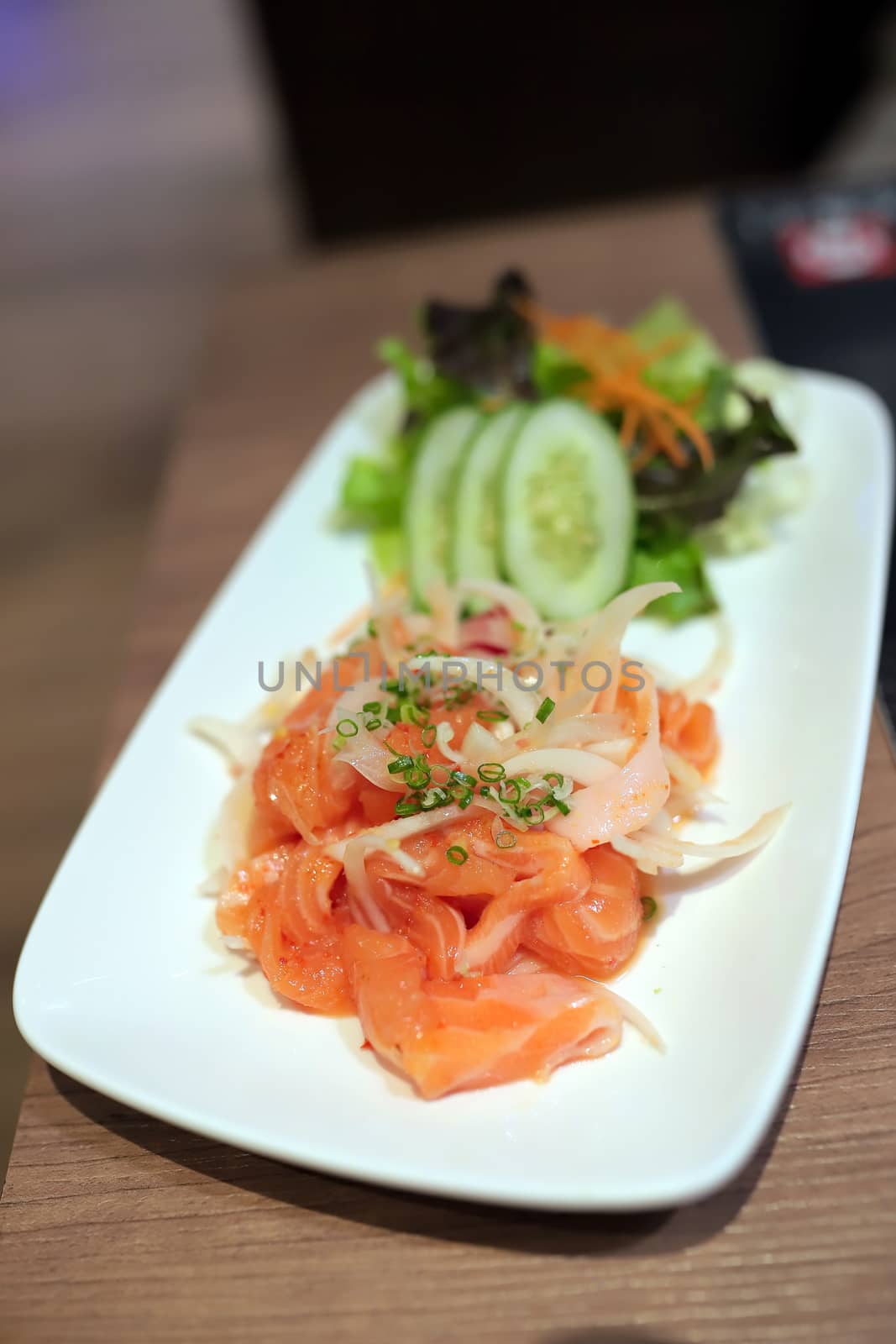 Salmon fillet Thai style spicy salad in white plate on wooden table in Japanese restaurant. Selective focus.
