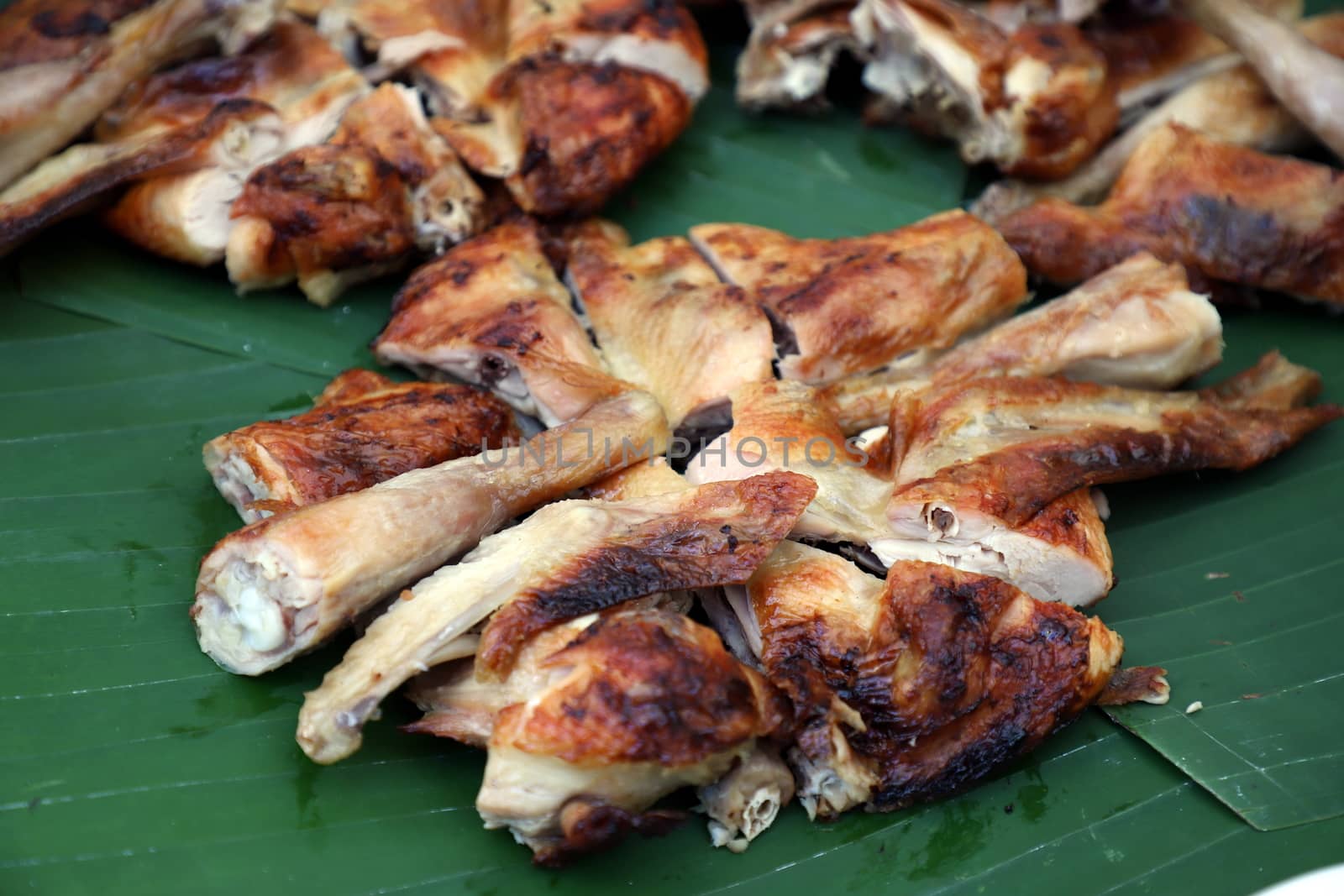 Grilled chicken cut into pieces Perfectly cooked, looks delicious. Nicely arranged on banana leaves. Selective focus. by joker3753