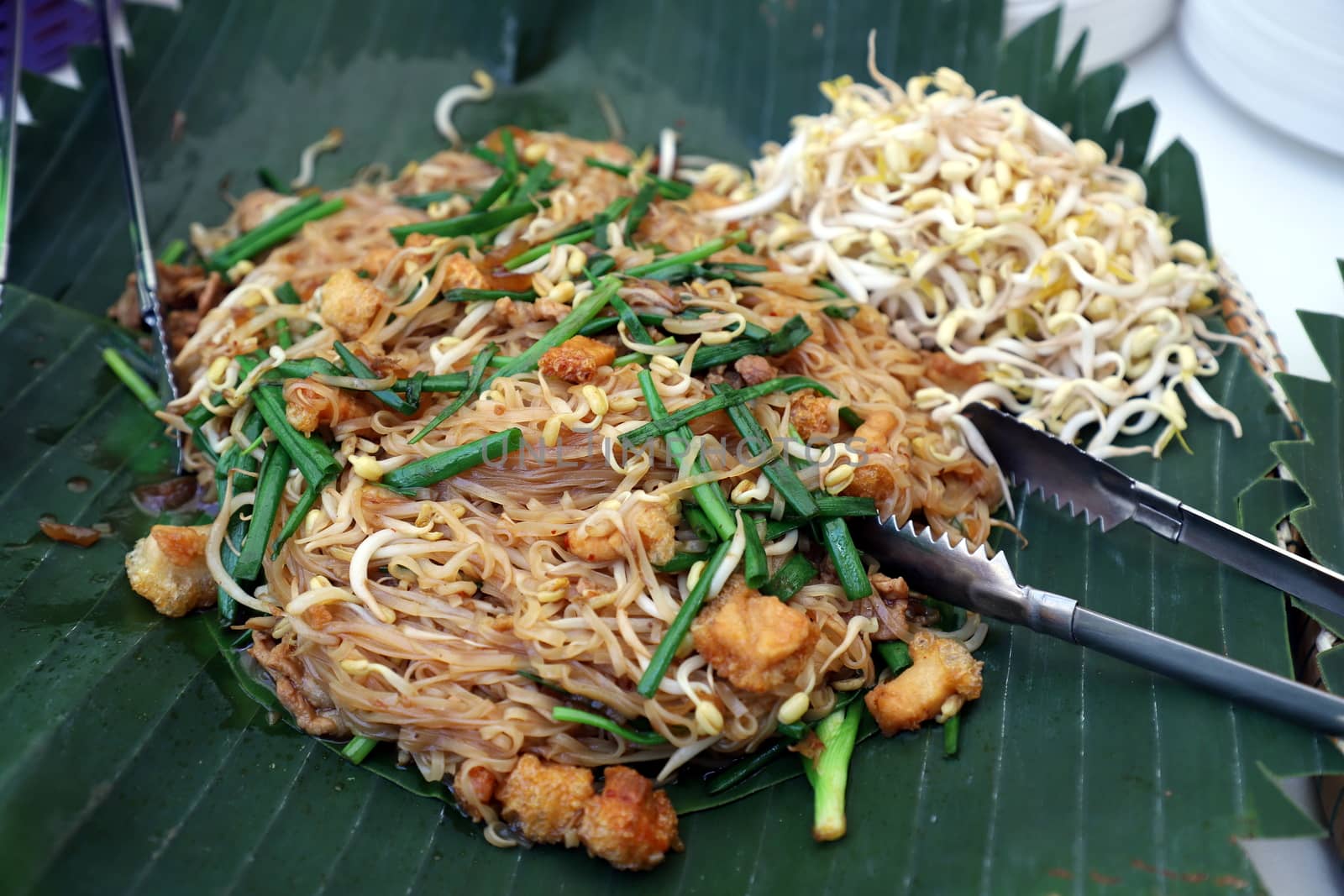 Korat Pad Mee is a local dish from Nakhon Ratchasima, Thailand, looks similar to Pad Thai in the central region on banana leaves, with a stainless steel tongs placed next to it. Selective focus.