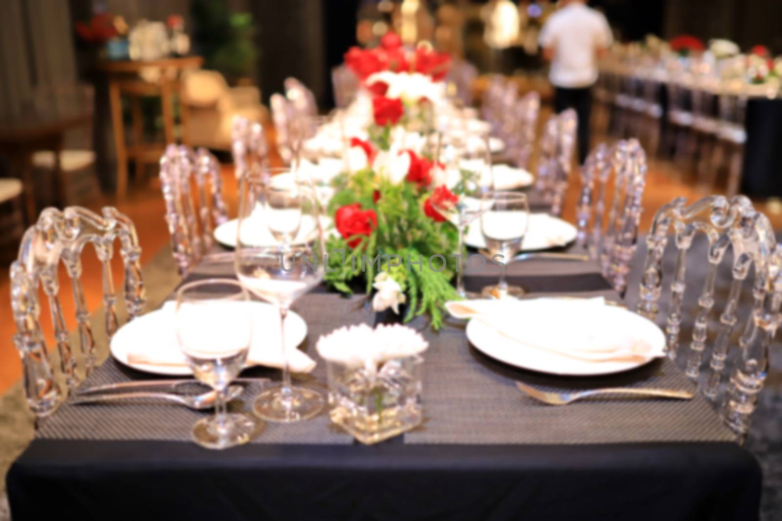 A blurred image of a dinner table with red roses. And green decorative leaves by joker3753