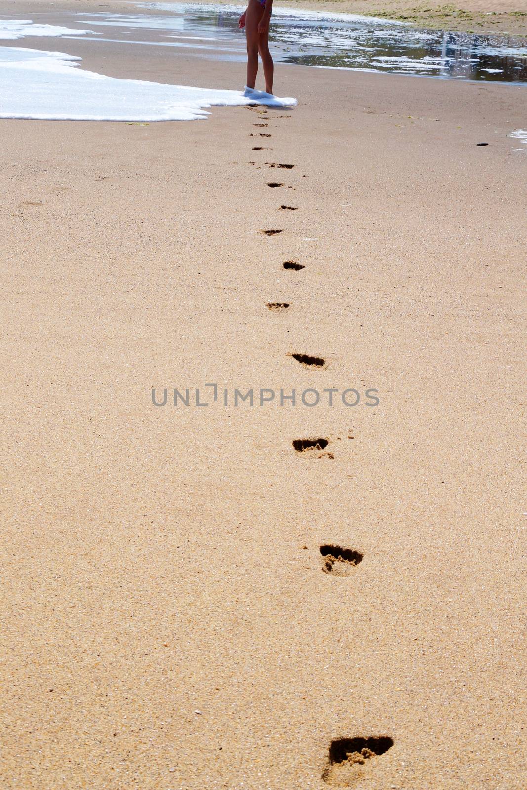 feet of a young girl walk barefoot on a wet beach, leaving footprints in the sand by Annado