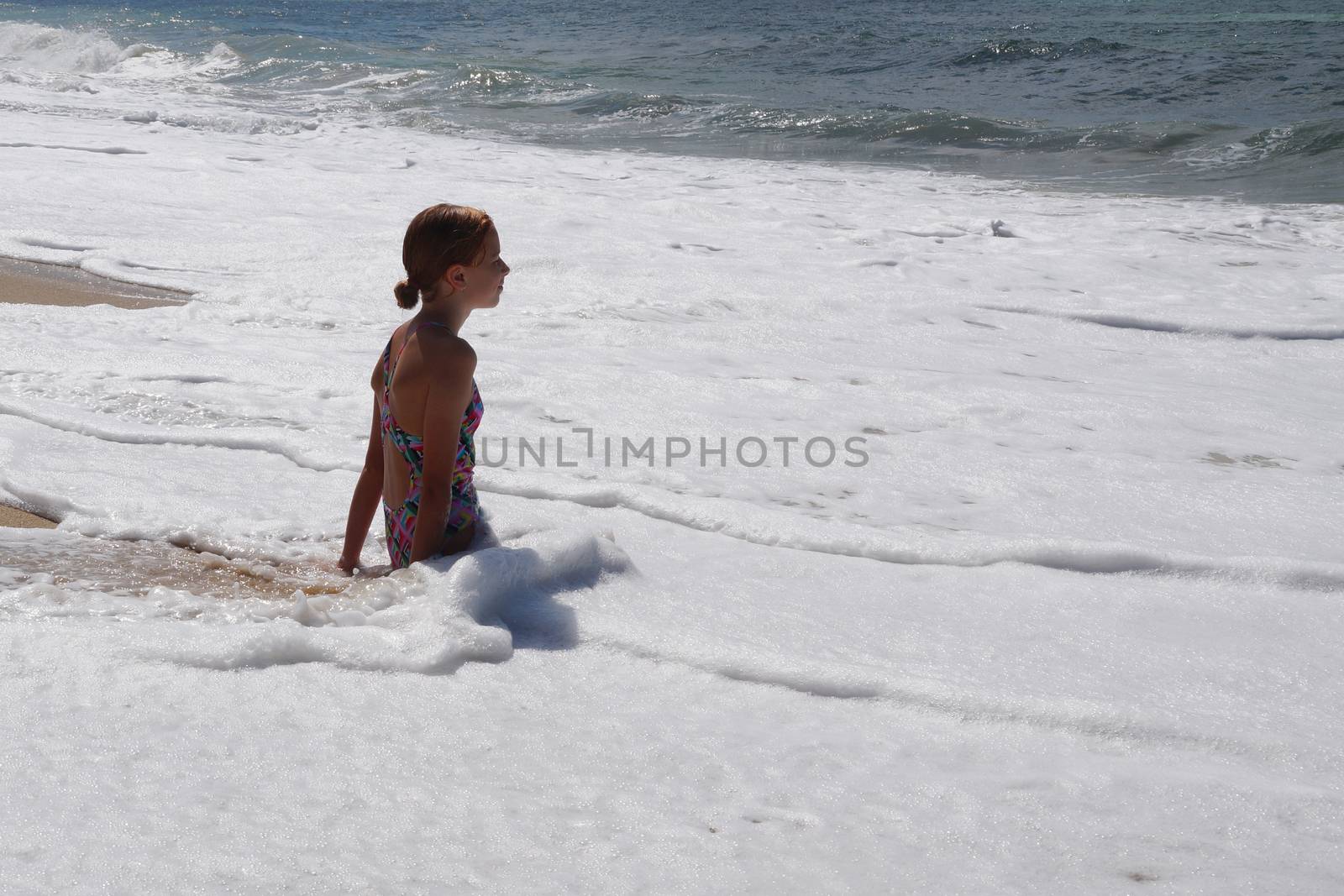 teenage girl sitting in white sea foam and looking at the sea.