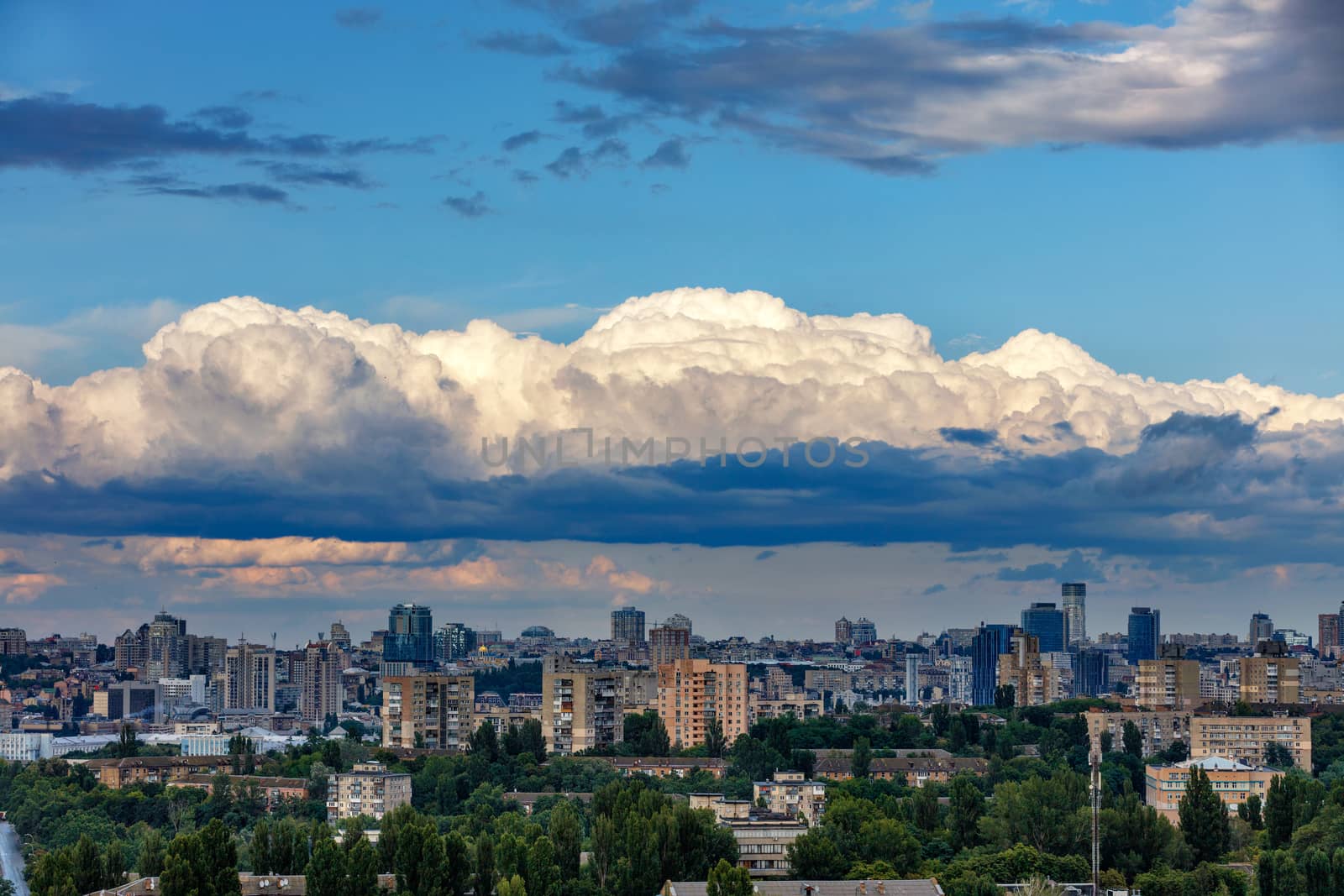 A dense cloud hung at dawn over the sleeping city, the sun's rays illuminate the top caps of white clouds. by Sergii