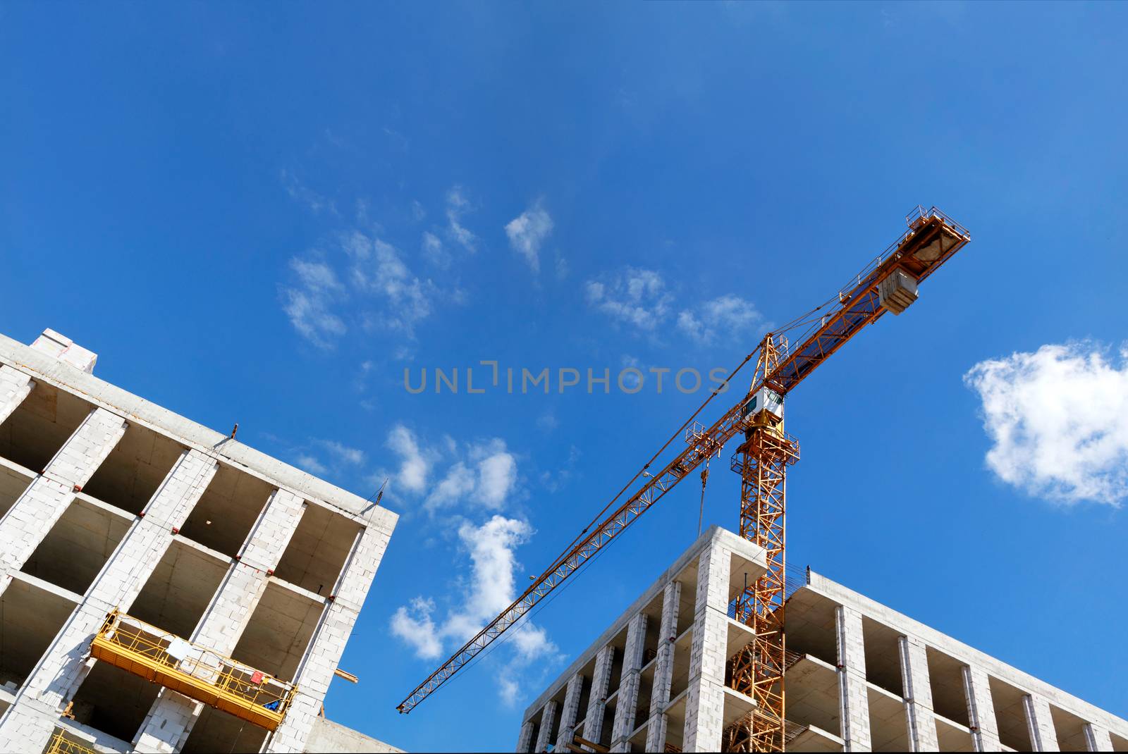 Monolithic frame concrete construction and tower cranes at the construction site of a multi-storey residential building against the blue skyand white clouds, copy space.
