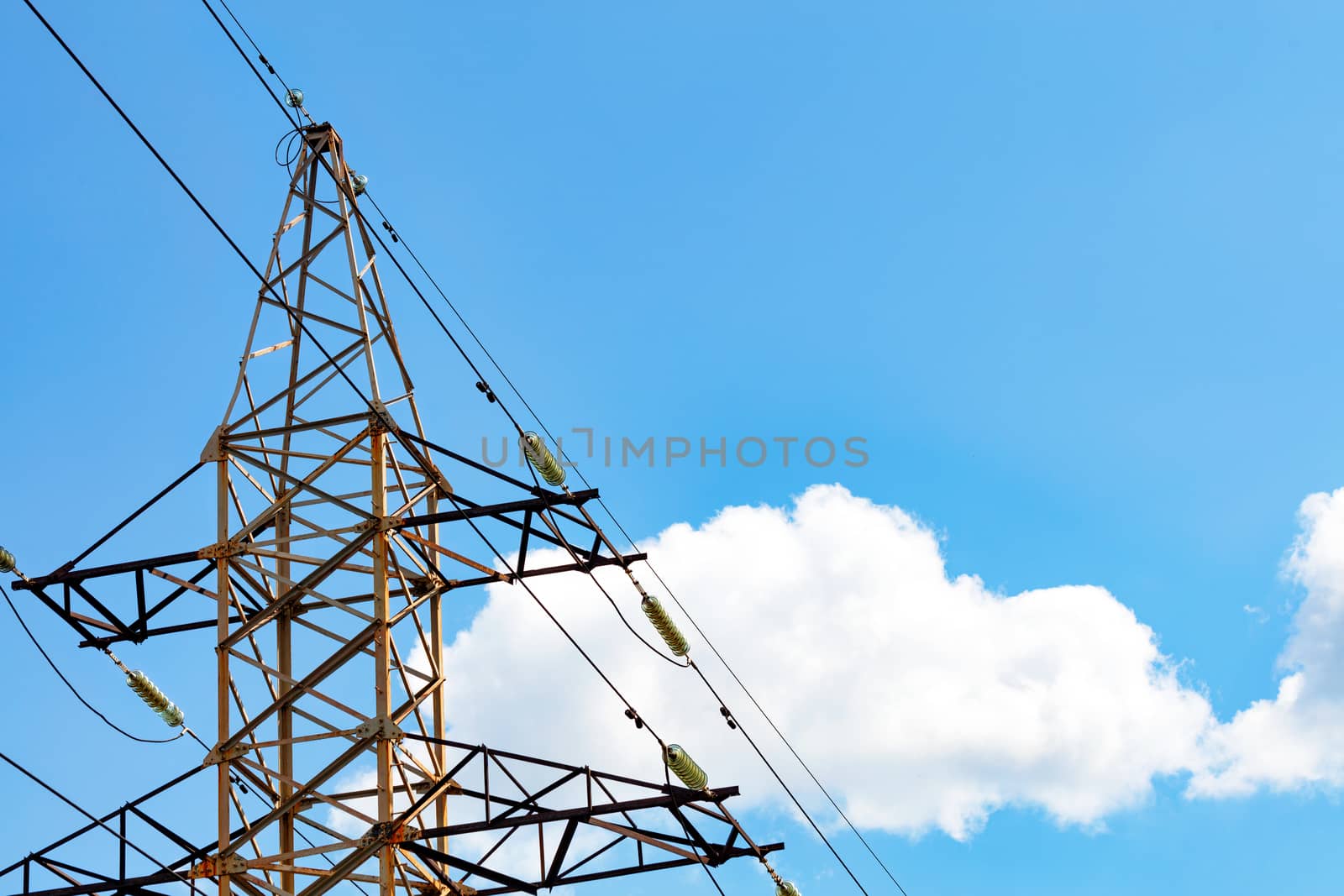 A metal power line support with insulators and wires used to support an overhead power line against white cloud and blue sky background, copy space.