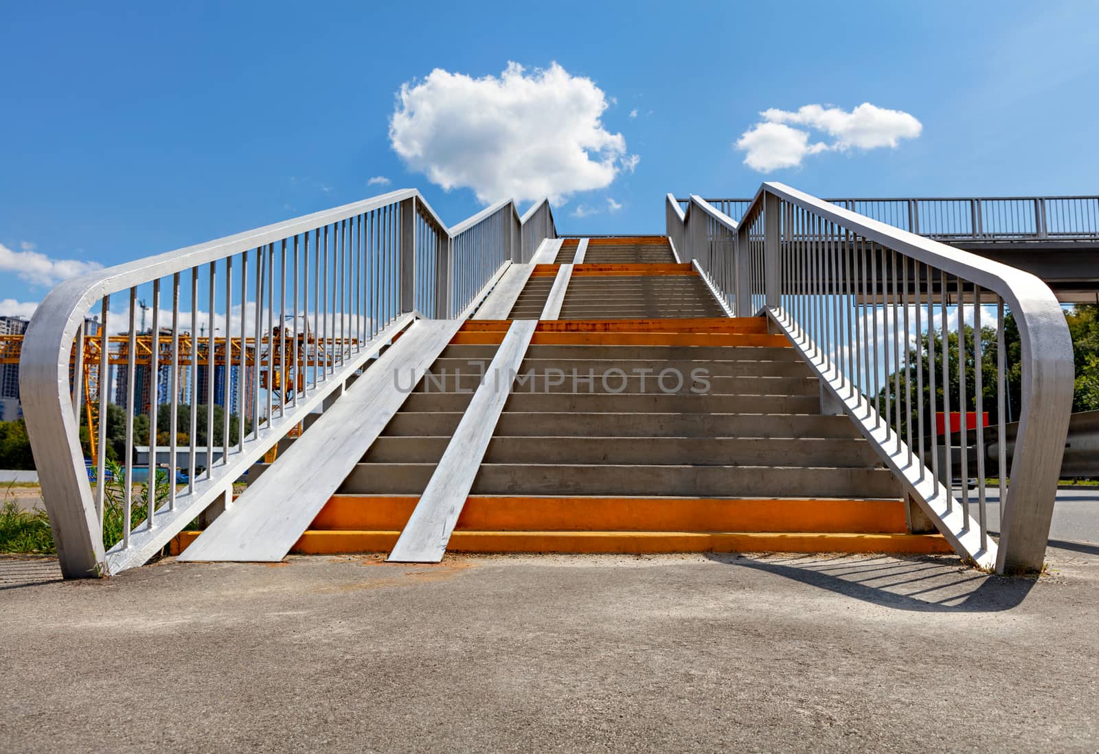 Wide entrance angle of a pedestrian crossing staircase over a highway against a background of blue sky and white clouds, low angle view, copy space.