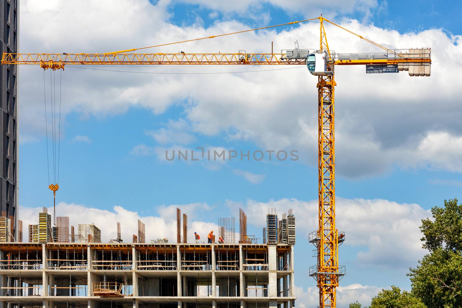 Tower crane works at the construction site of a multi-storey residential building against a blue cloudy sky. Copy space.
