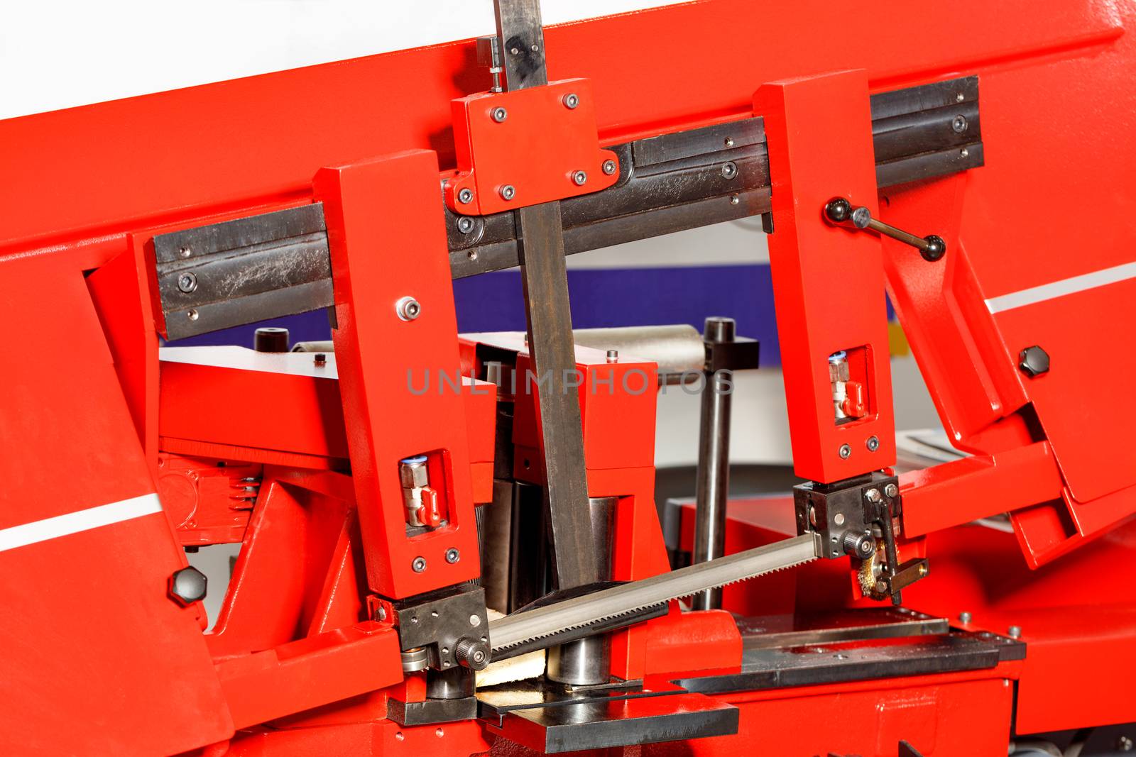 The sharp teeth of the band saw on the modern red metal working machine ensure high cutting accuracy thanks to the adjusting line. Close-up.