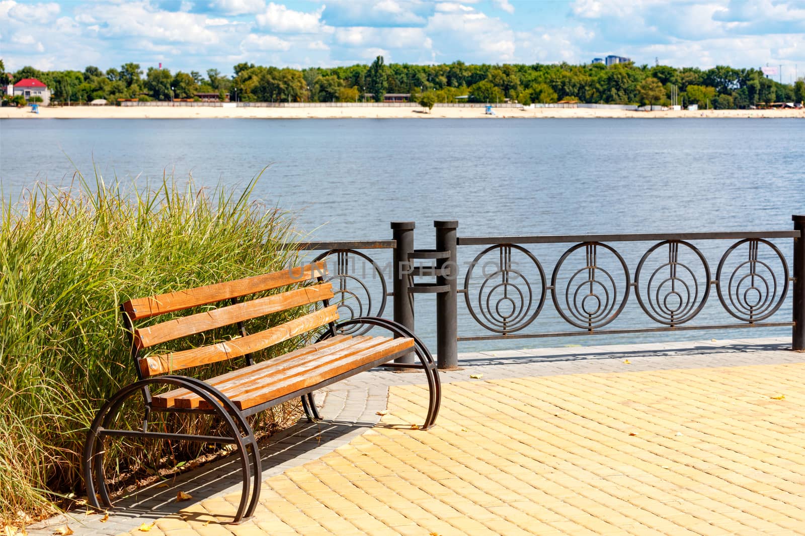 A wooden bench on the Dnipro embankment against the background of a wide river and a blurred sandy beach. by Sergii