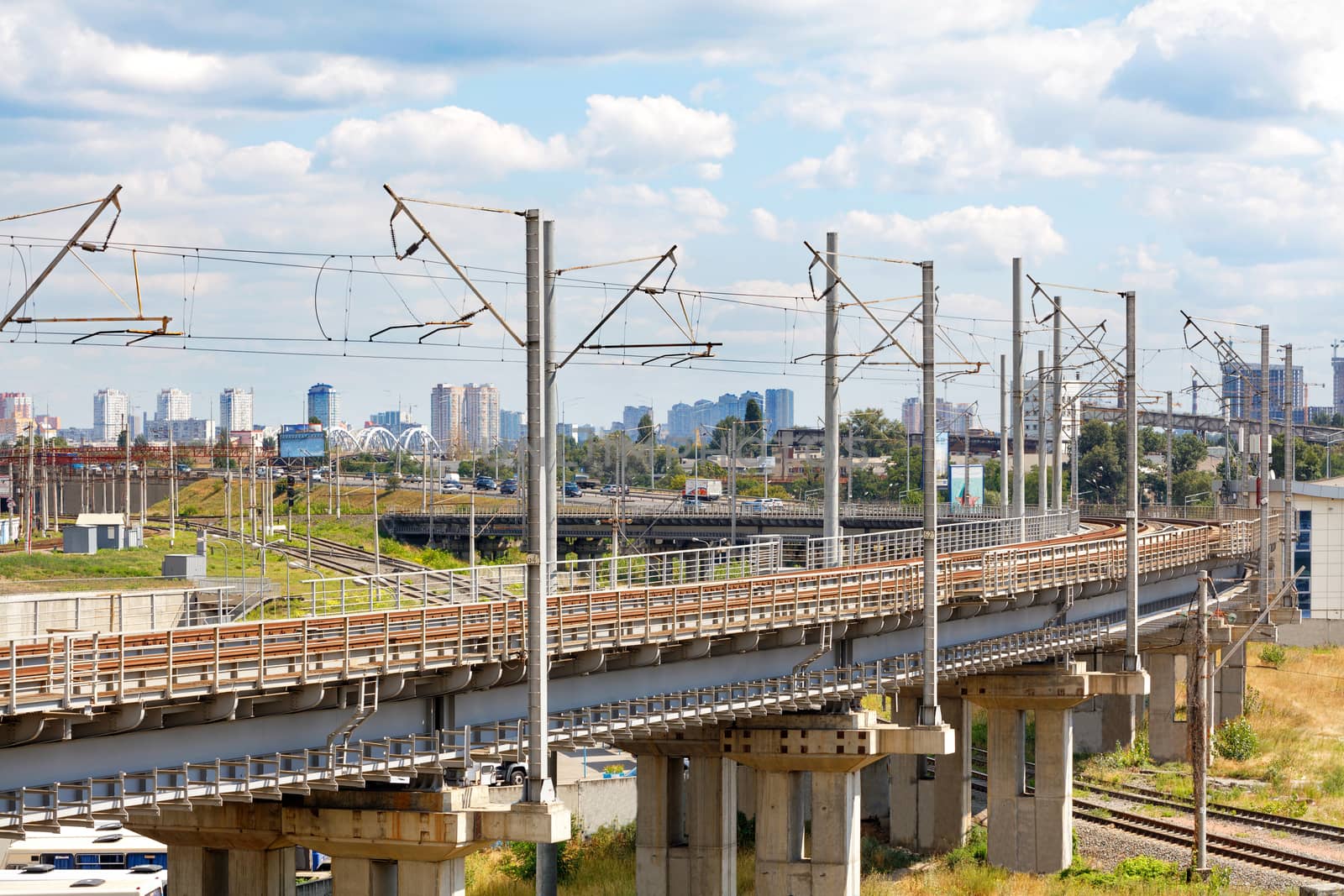 Perspective of a multi-channel and multi-level railway for electric trains with overhead power lines on a summer day against the backdrop of a blurred cityscape in the haze.