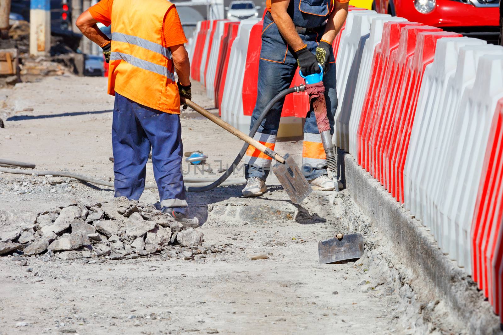 Workers repairing an old section of the road using a pneumatic jackhammer and shovels to remove worn parts of the road, copy space.