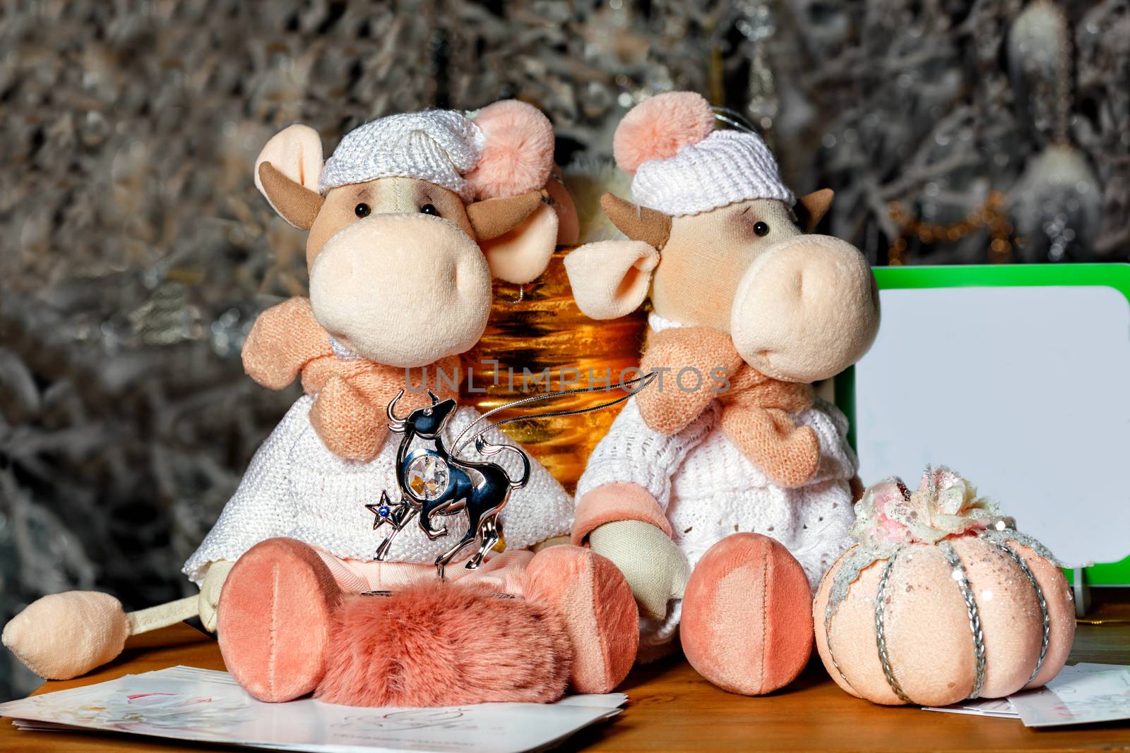 Two cute toy bulls as a symbol of the new year 2021 on a blurred bokeh background of golden garlands next to a pile of greeting cards and place for text.