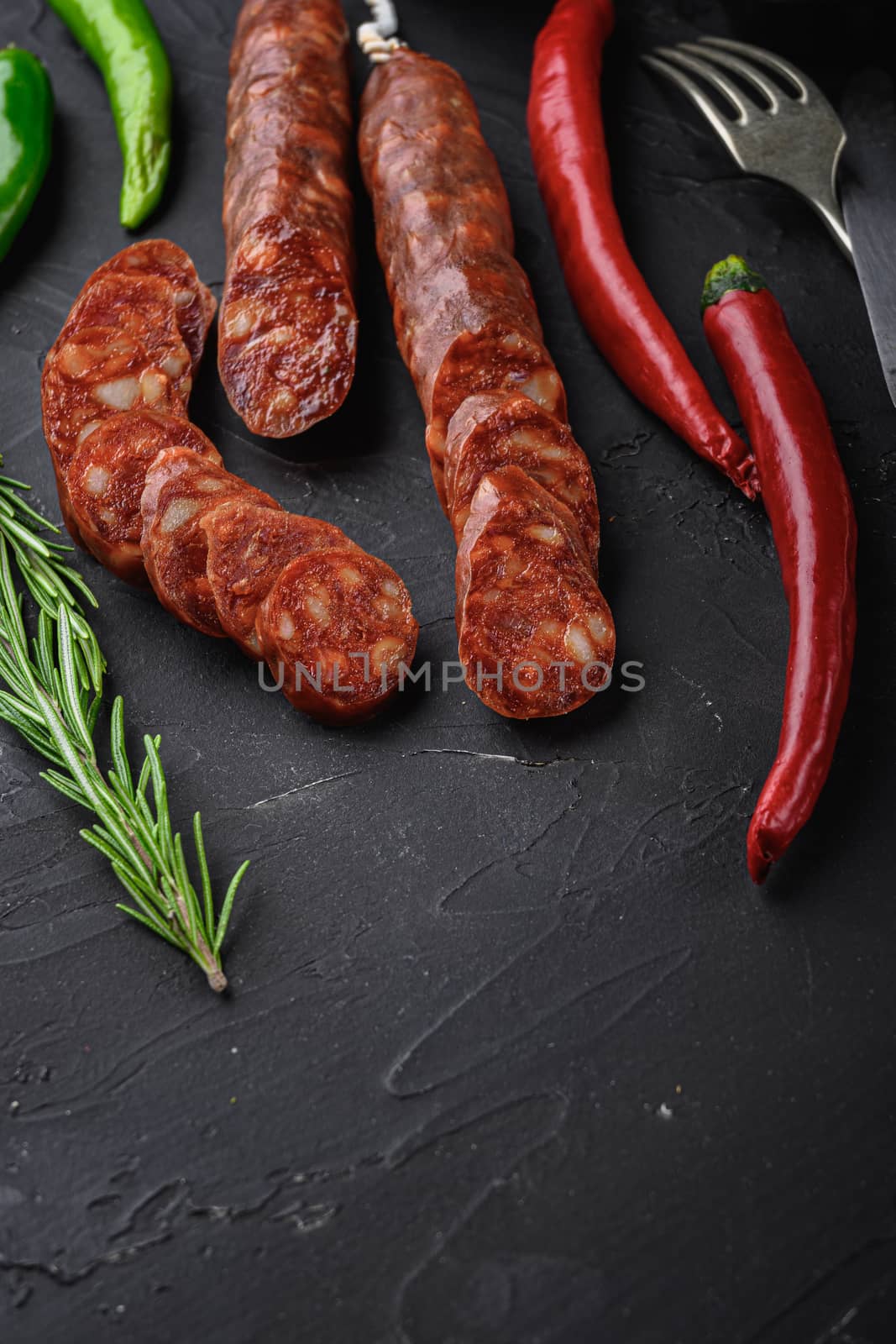 Spanish chorizo sausage slices with herbs and spices on black textured background with space for text.