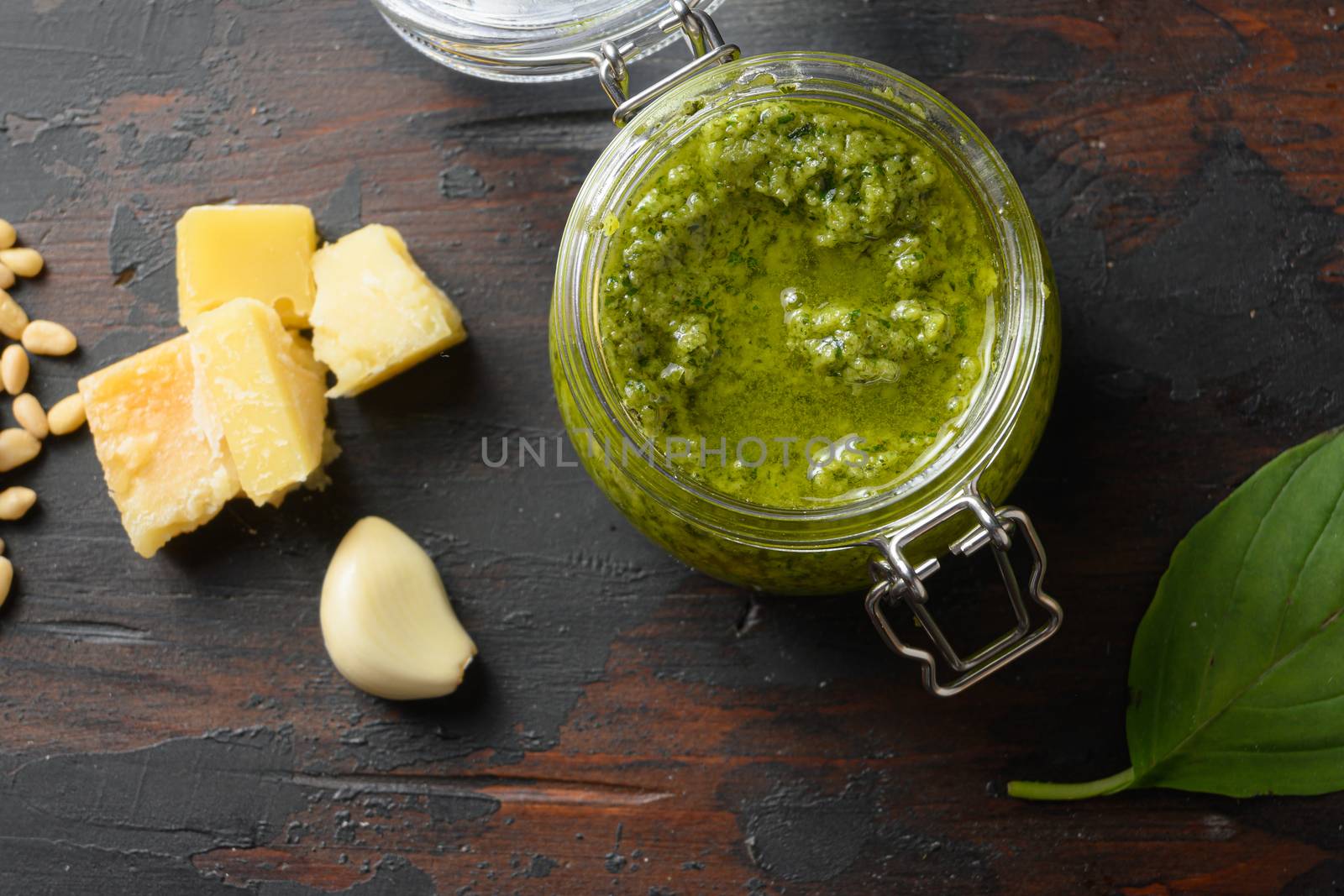 Pesto alla Genovese in glass jar with ingredients parmesan basil pine nuts. on dark wood table planks vintage side view.