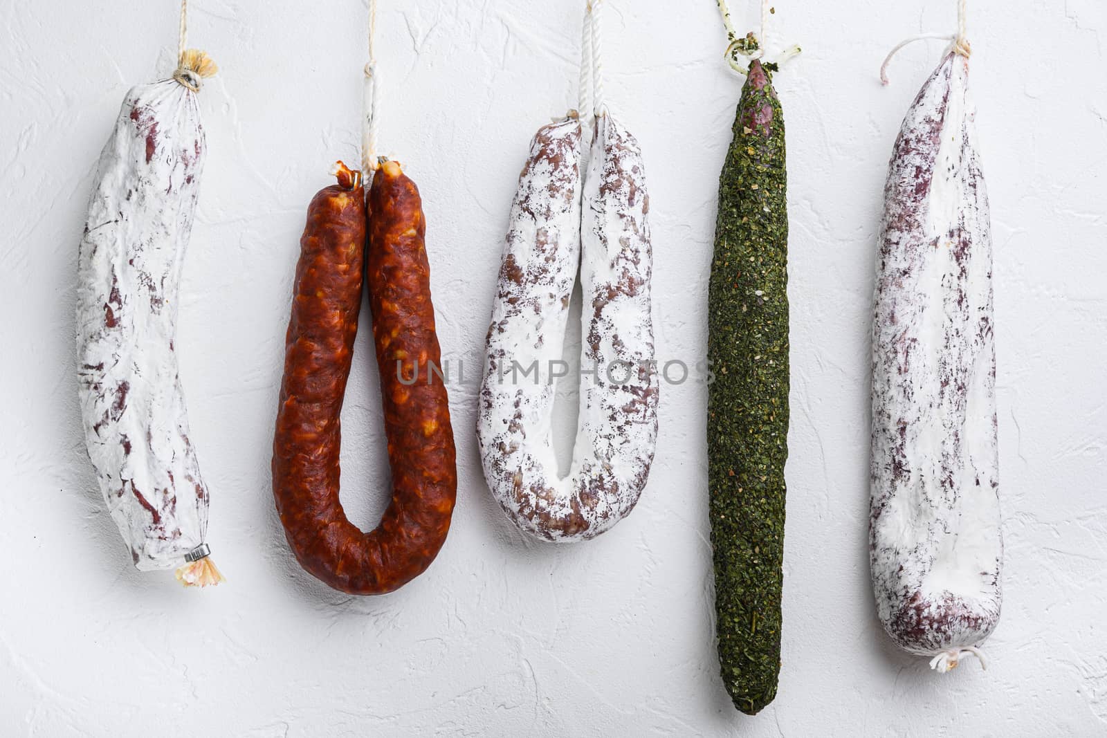 Traditional dry cured sausages meat hanging on white textured background.