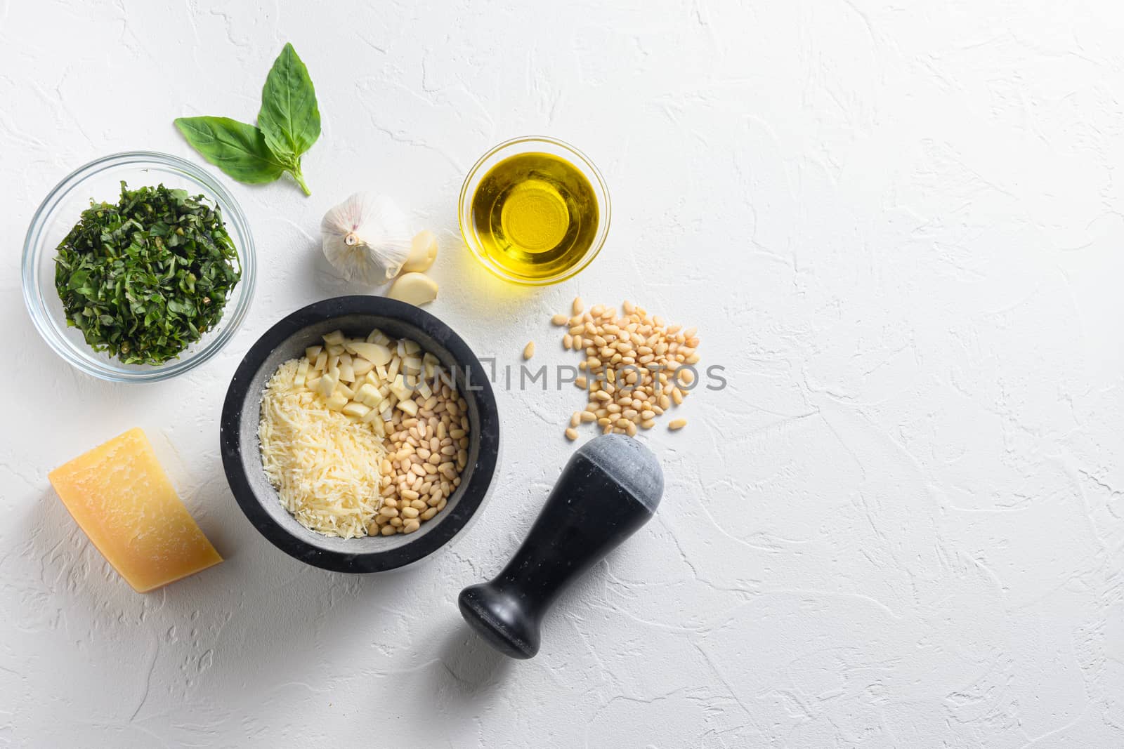 Pesto sauce cooking and mortar with ingredients . Basil, olive oil, parmesan, garlic, pine nuts. Top view with white stone surface space for your text top view