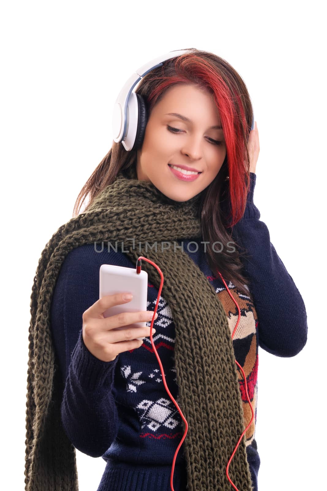 Beautiful smiling young woman wearing winter scarf with headphones listening to music, looking at her mobile phone, isolated on white background. Season, technology and people concept.