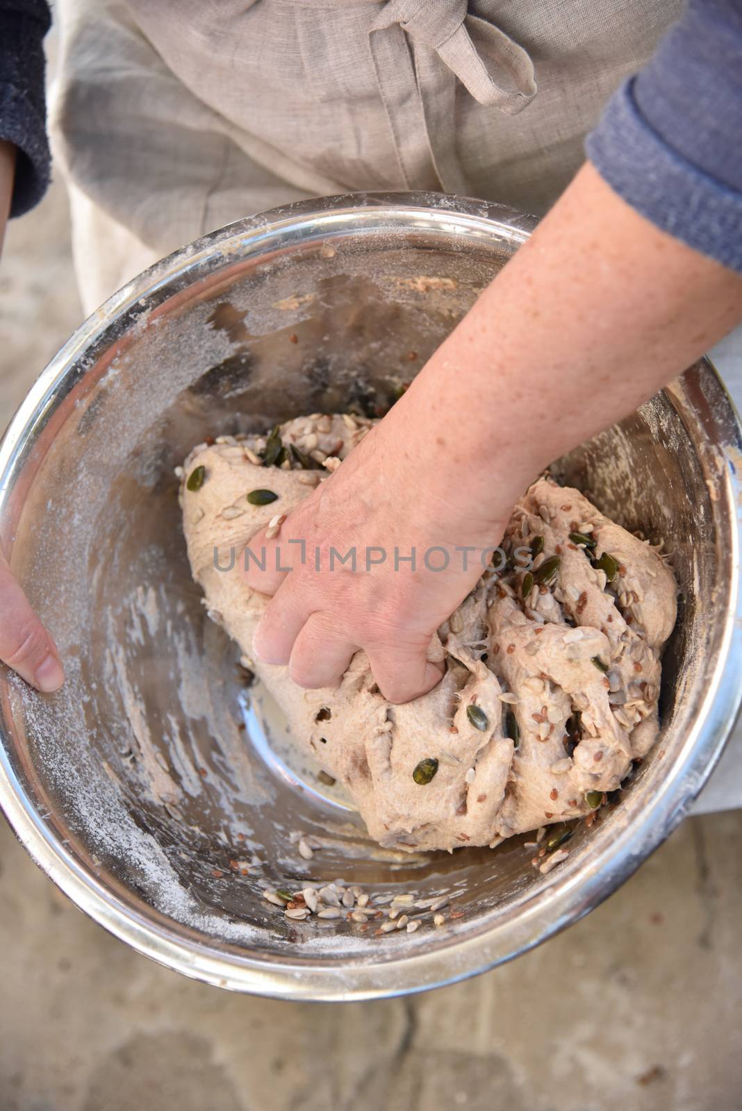 A person holding a bowl of food. Handmade bread dough in a stainless steel bowl. Close up of a baker kneading bread dough in a metal bowl. High quality photo