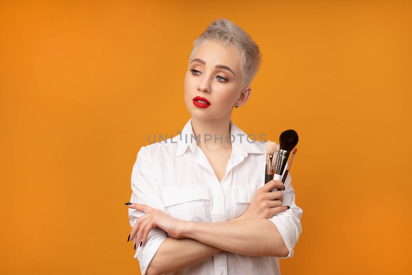 Close up portrait makeup artist. Make up courses. Concept of self visage masterclasess. Fashion professional. Woman hold makeup brushes on the hands. Studio shot on the orange color background