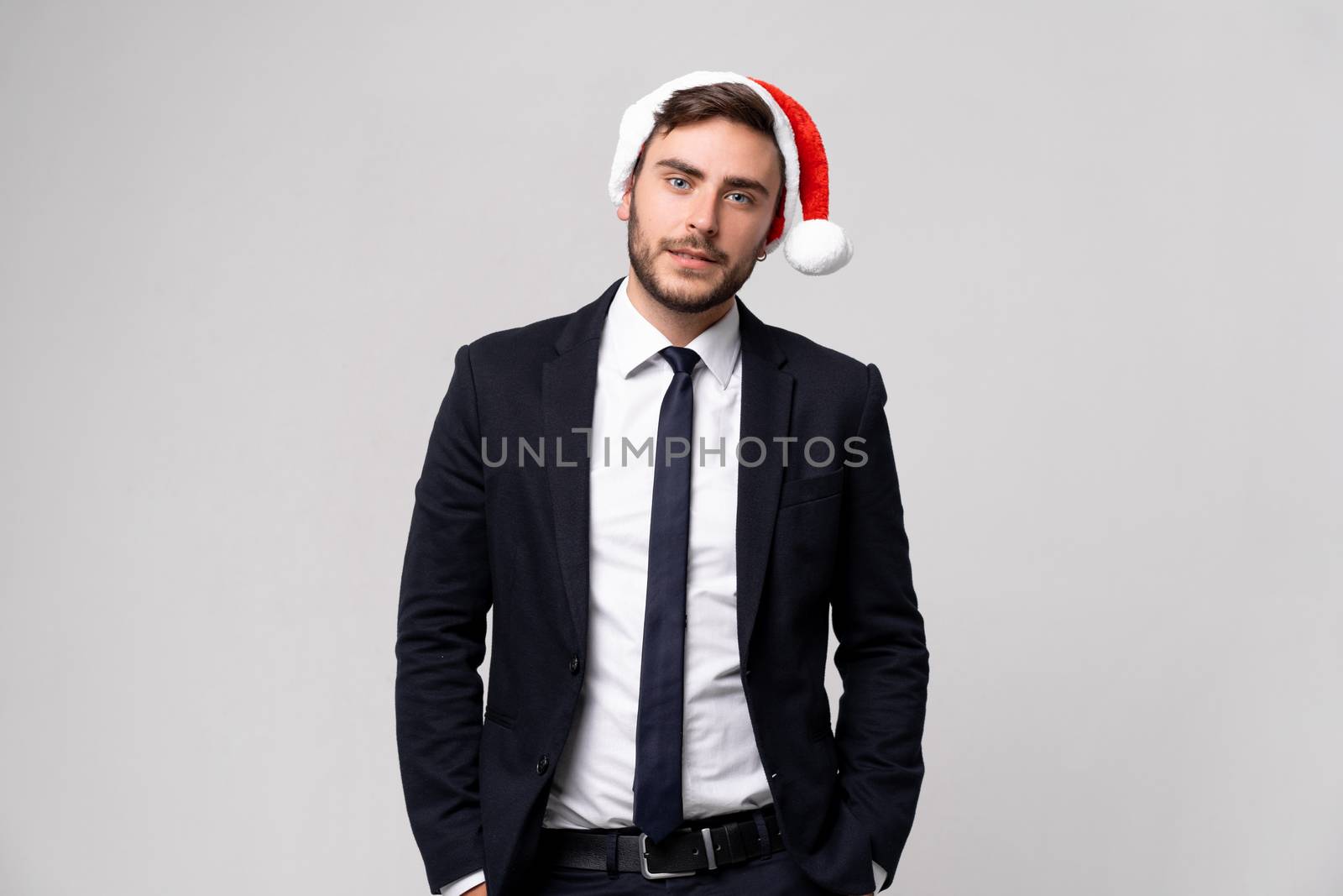 Young handsome caucasian guy in business suit and Santa hats stands on white background in studio teeth smilie. Close up portrait business person with Christmas mood Holiday banner