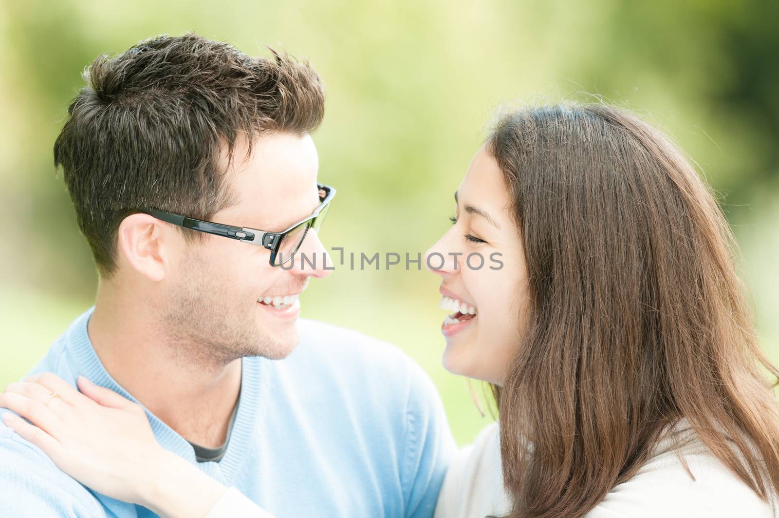 Portrait of beautiful romantic couple. People dating in park. Pretty woman with man in glasses and blue pullover. Green nature as background. Young positive family having leisure time outside.