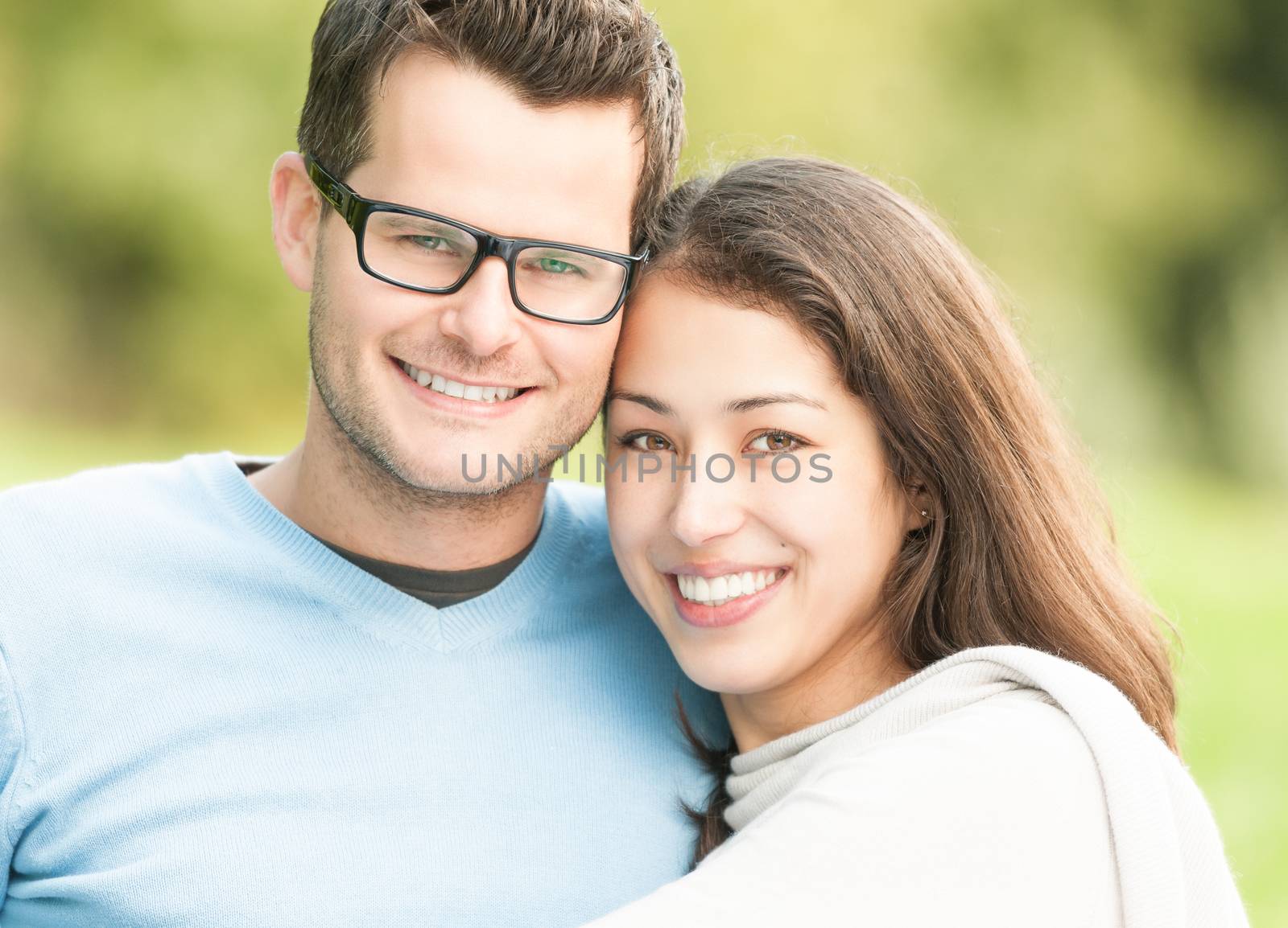 Portrait of beautiful romantic couple. People dating in park. Pretty woman with man in glasses and blue pullover. Green nature as background. Young positive family having leisure time outside.