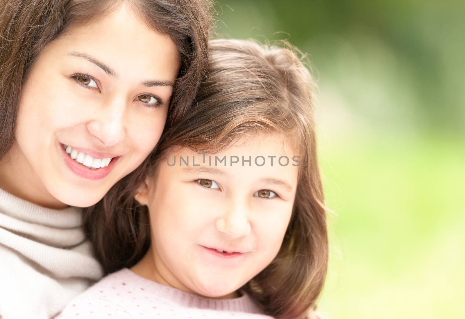 Beautiful and happy young mother with her small daughter outdoors. Both woman and small girl happy and smiling, green park in background.