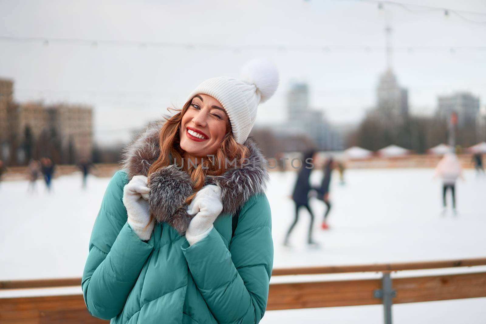 Beautiful lovely middle-aged girl curly hair warm winter jackets white knitted hat glove stands ice rink background Town Square Christmas mood lifestyle Happy holiday woman snowy day Winter leisure