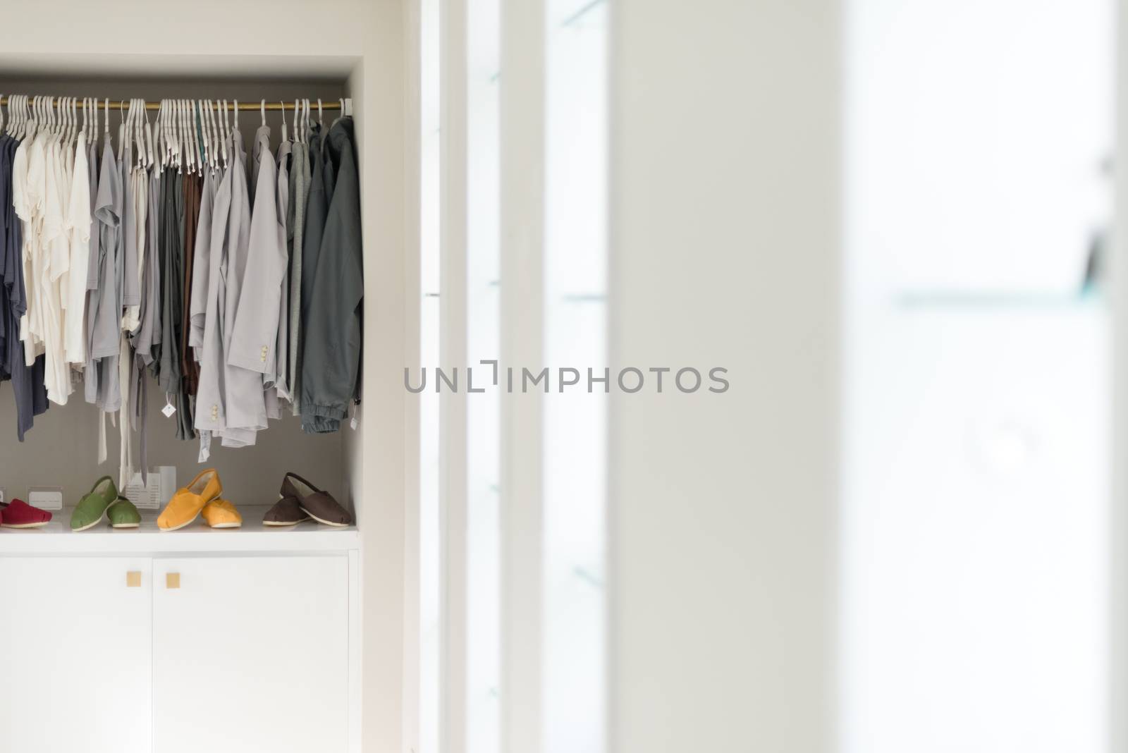 Row of new casual clothing on hangers at shop with four colorful pairs of shoes under it. Clothes presented as in wardrobe. Apparel ready for sale. Going shopping. Trade and commerce.