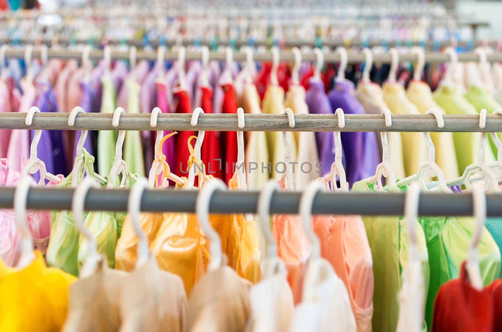 Rows of new colorful clothing on hangers at shop in foreground and background. Great choice of casual clothes of different colors. Apparel ready for sale. Going shopping. Trade and commerce.