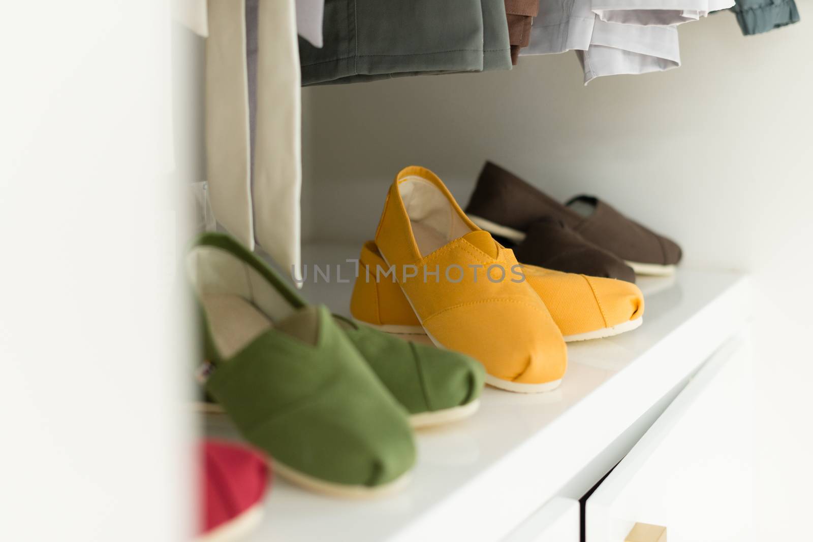 Row of new casual clothing on hangers at shop with four colorful pairs of shoes under it. Clothes presented as in wardrobe. Apparel ready for sale. Going shopping. Trade and commerce.