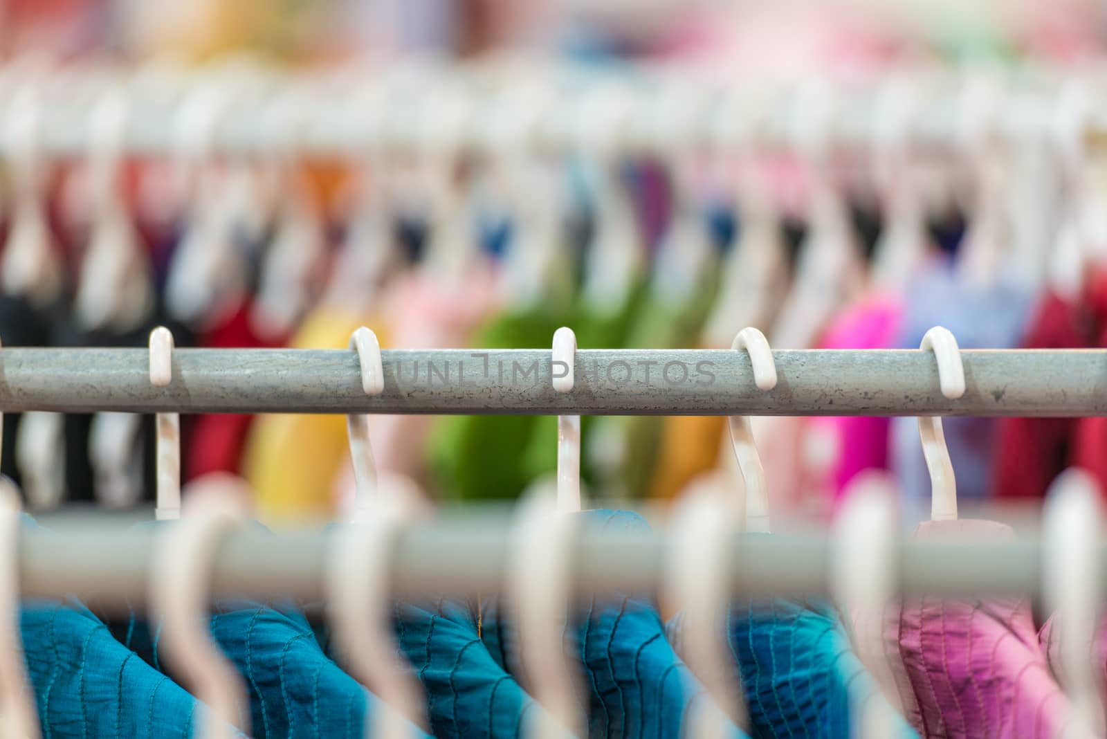 Rows of colorful clothes on hangers at shop. by Yolshin